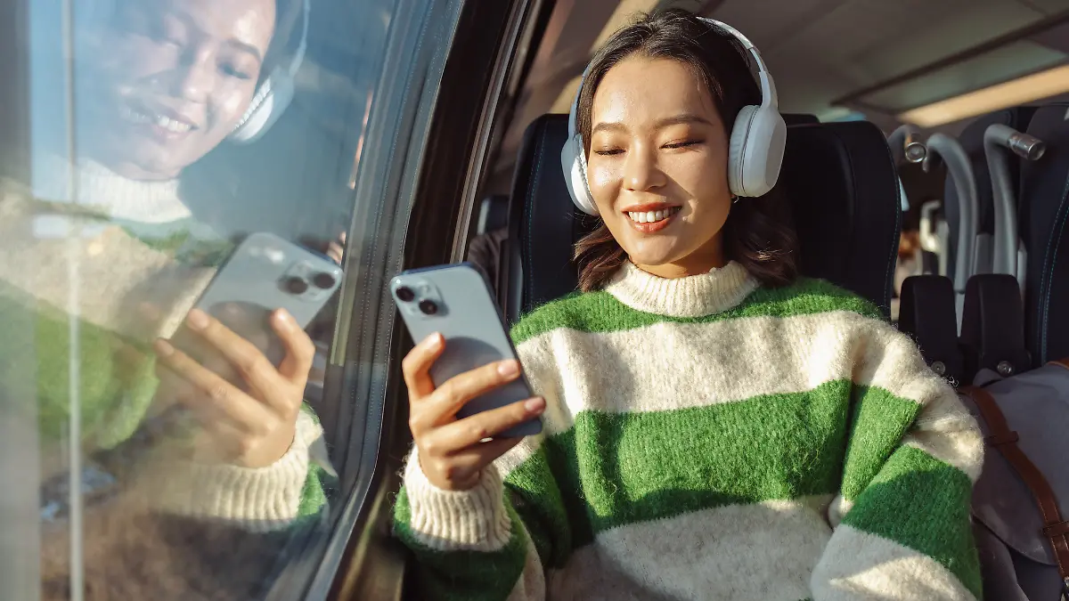 Eine junge asiatische Frau sitzt im Zug und schaut auf ihr Handy. Sie ist glücklich.