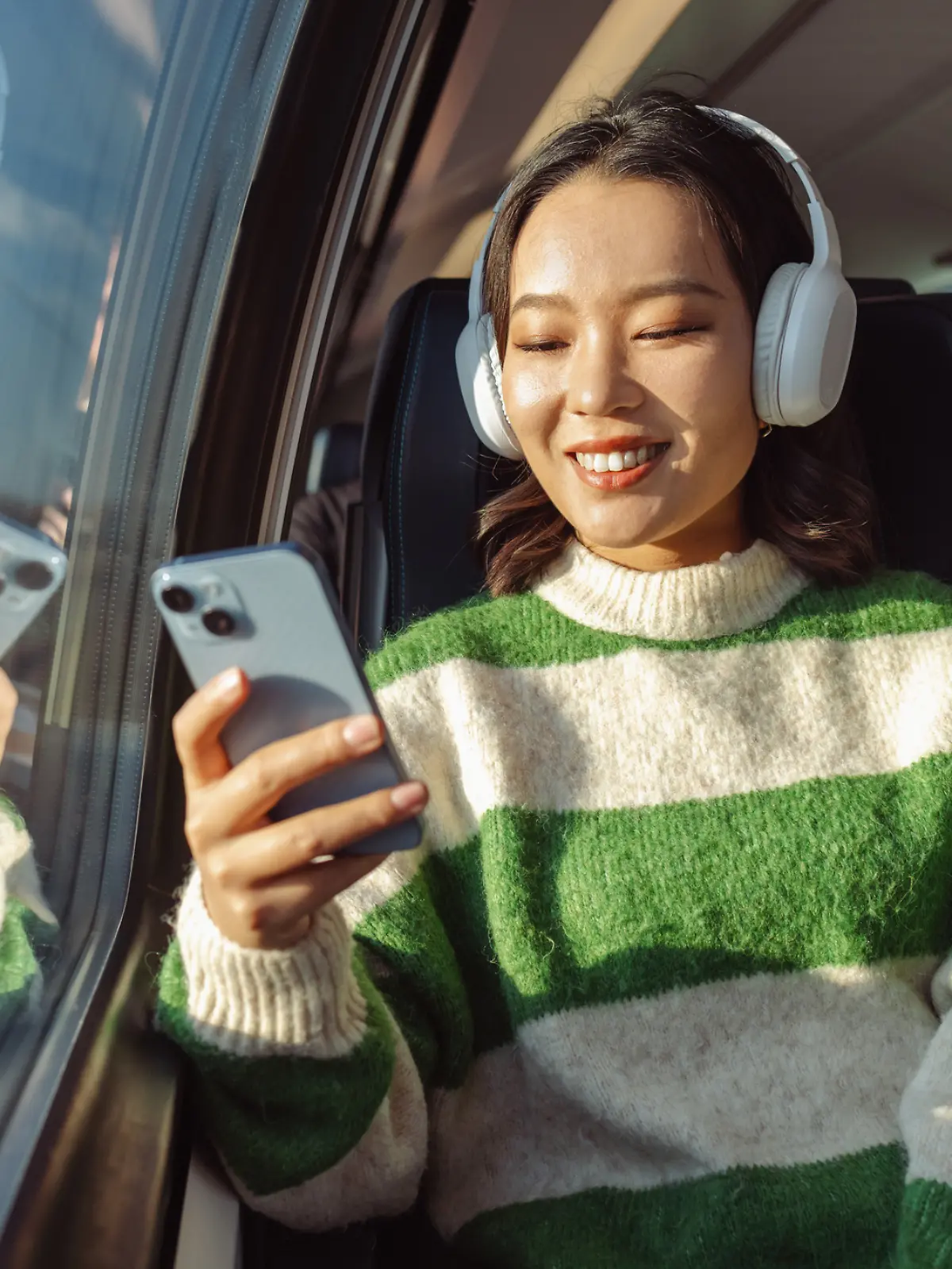 Eine junge asiatische Frau sitzt im Zug und schaut auf ihr Handy. Sie ist glücklich.