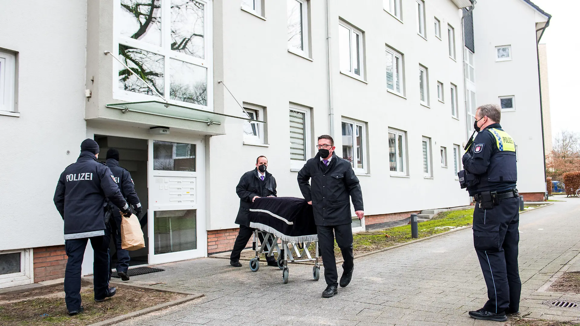 ARCHIV - 08.02.2021, Hamburg: Bestatter transportieren im Februar im Hamburger Stadtteil Bramfeld einen Sarg aus einem Mehrfamilienhaus ab. Ein Mann soll dort am vorherigen Abend seine Mutter umgebracht haben. Etwa einen Tag zuvor soll er auch seine Freundin getötet haben. Nun beginnt das Sicherungsverfahren gegen den 29-Jährigen, dem Totschlag und heimtückischer Mord vorgeworfen wird. (zu dpa: «Mutter und Freundin getötet? - Prozessbeginn gegen 29-Jährigen») Foto: Daniel Bockwoldt/dpa +++ dpa-Bildfunk +++