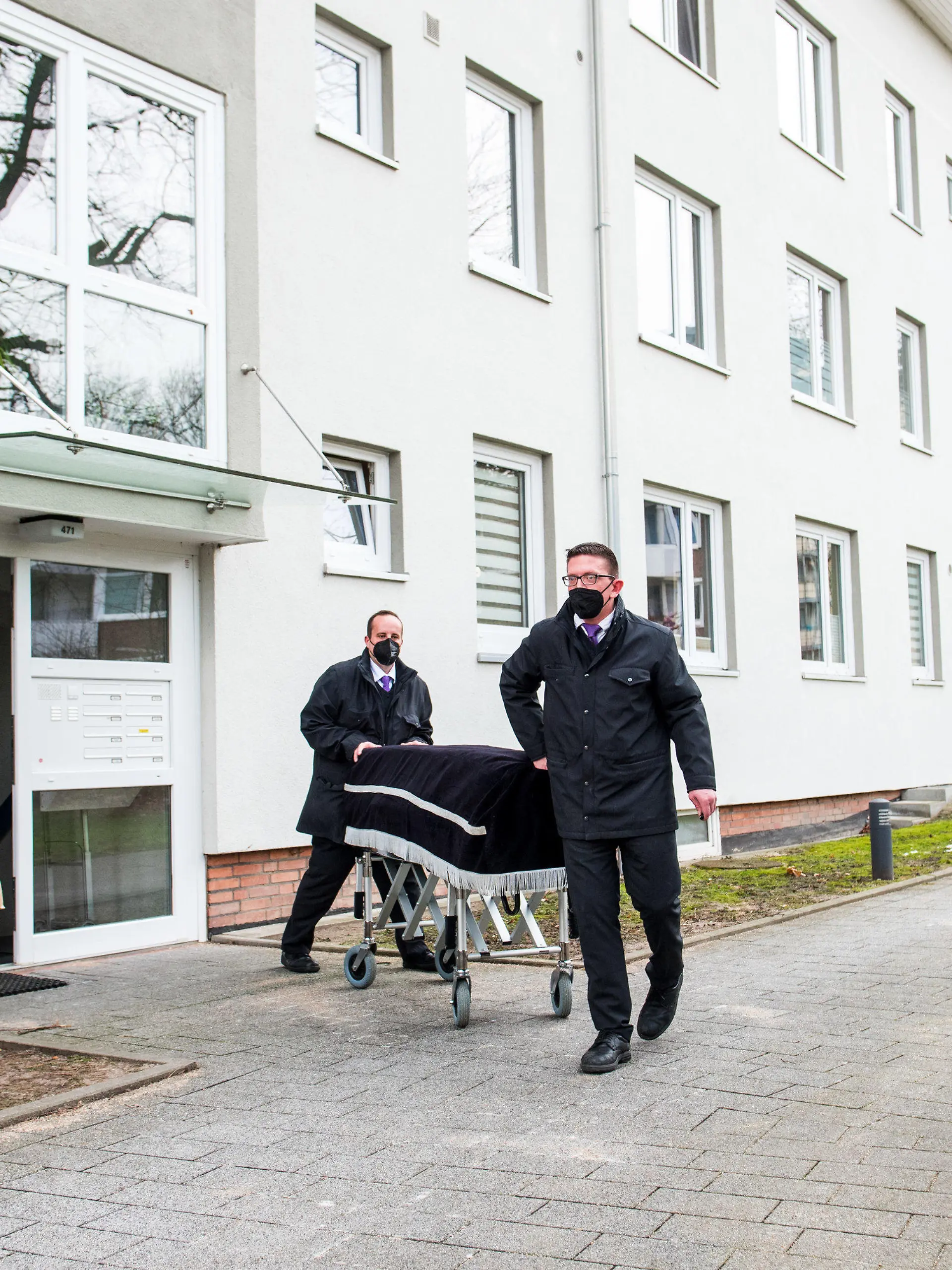 ARCHIV - 08.02.2021, Hamburg: Bestatter transportieren im Februar im Hamburger Stadtteil Bramfeld einen Sarg aus einem Mehrfamilienhaus ab. Ein Mann soll dort am vorherigen Abend seine Mutter umgebracht haben. Etwa einen Tag zuvor soll er auch seine Freundin getötet haben. Nun beginnt das Sicherungsverfahren gegen den 29-Jährigen, dem Totschlag und heimtückischer Mord vorgeworfen wird. (zu dpa: «Mutter und Freundin getötet? - Prozessbeginn gegen 29-Jährigen») Foto: Daniel Bockwoldt/dpa +++ dpa-Bildfunk +++
