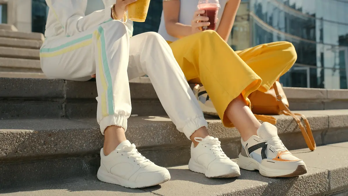 Zwei Frauen sitzen auf der Treppe und ihre weißen Sneaker sind im Fokus. 