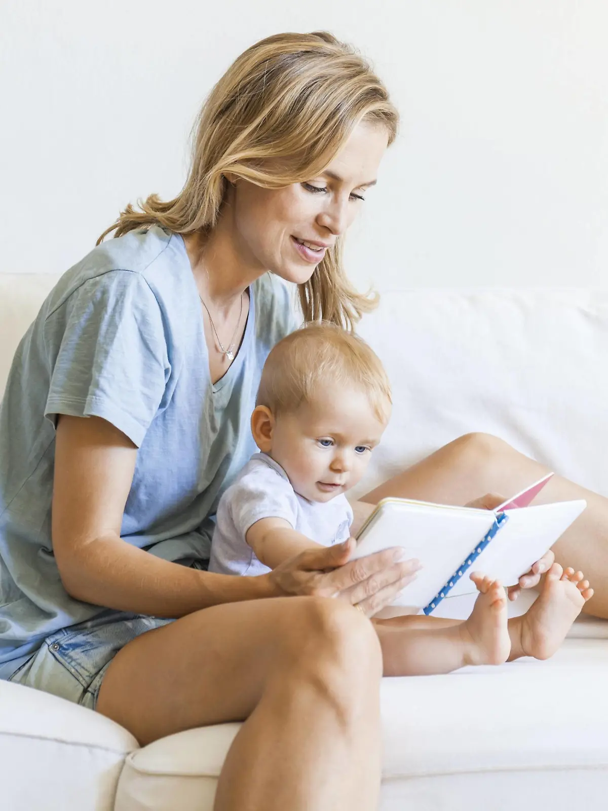 Mother and baby girl sitting on couch looking at picture book model released Symbolfoto property released PUBLICATIONxINxGERxSUIxAUTxHUNxONLY TCF05872  