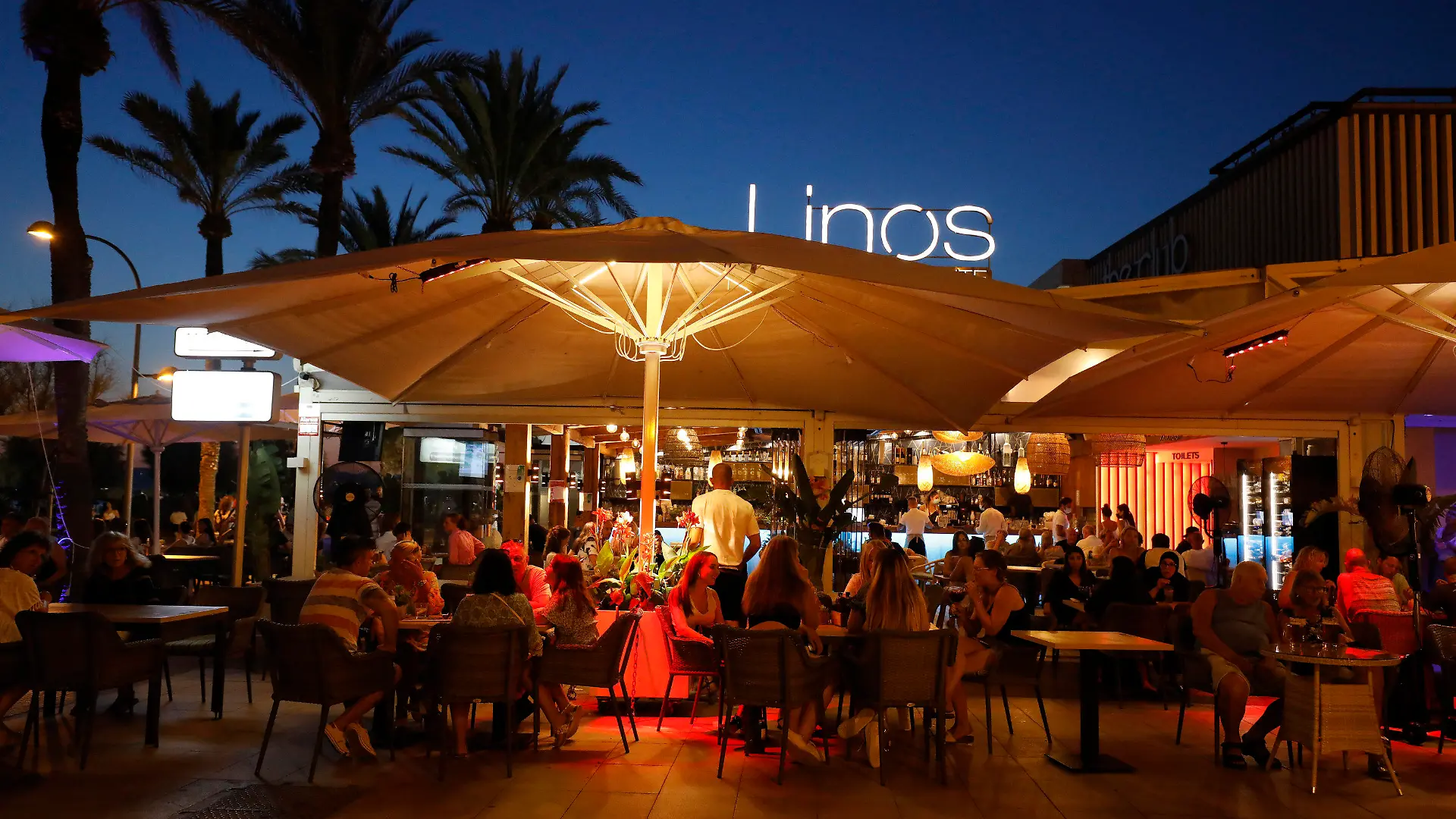 ARCHIV - 22.07.2021, Spanien, Palma de Mallorca: Menschen sitzen in einer Bar an der Strandpromenade von Palma. Angesichts fallender Corona-Zahlen werden die Corona-Restriktionen auf der bei Deutschen beliebten Urlauberinsel Mallorca weiter gelockert. Ab 07.09.2021 dürfen wieder Personen aus verschiedenen Haushalten zu nächtlichen Partys zusammenkommen, teilte die Regionalregierung mit. (zu dpa "Mallorca lockert Corona-Regeln: Nächtliche Partys wieder erlaubt") Foto: Clara Margais/dpa +++ dpa-Bildfunk +++