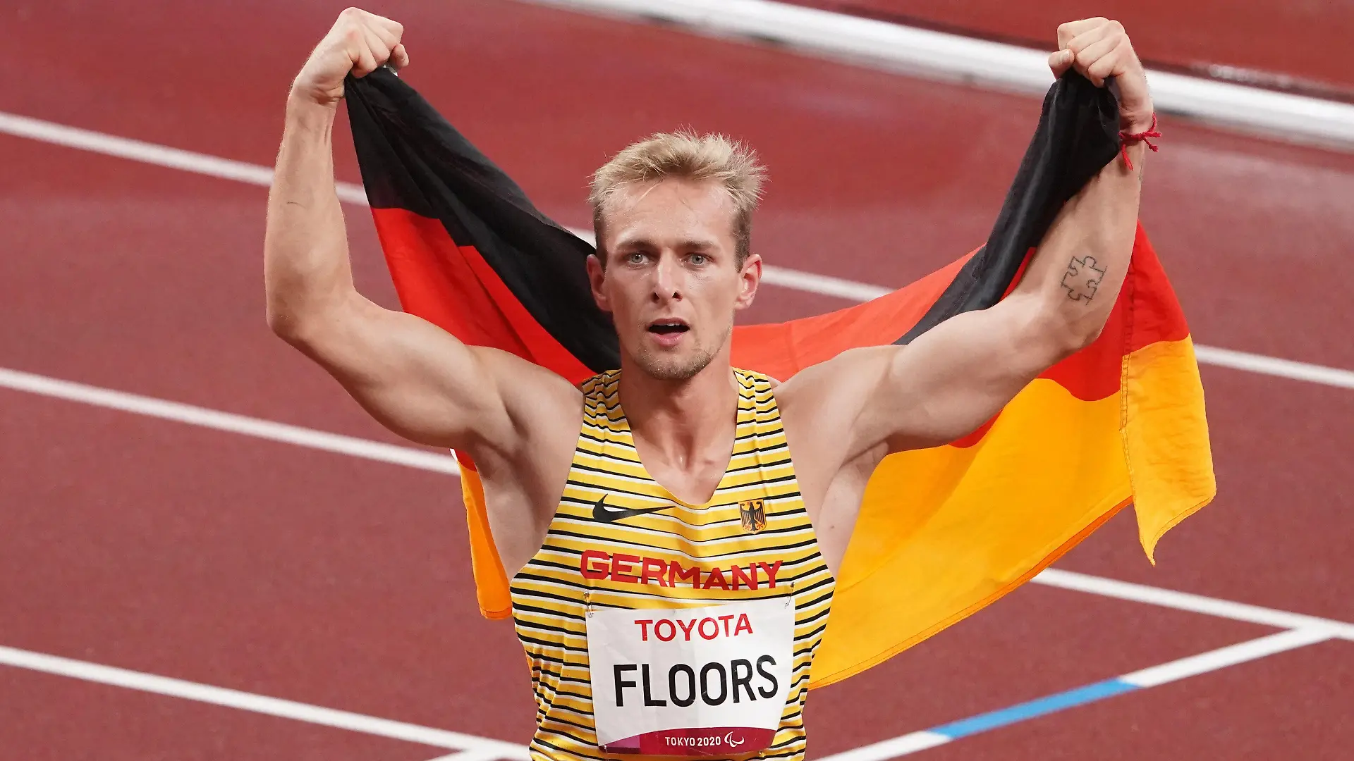 03.09.2021, Japan, Tokio: Paralympics: Leichtathletik, 400 Meter Männer, T62 Finale, im Olympiastadion. Goldmedaillen-Gewinner Johannes Floors aus Deutschland jubelt nach seinem Sieg und neuem Weltrekord mit einer Deutschlandfahne auf den Schultern. (zu dpa "Zielsichere Hiltrop, Raser Floors: Die Gesichter der Paralympics") Foto: Marcus Brandt/dpa +++ dpa-Bildfunk +++