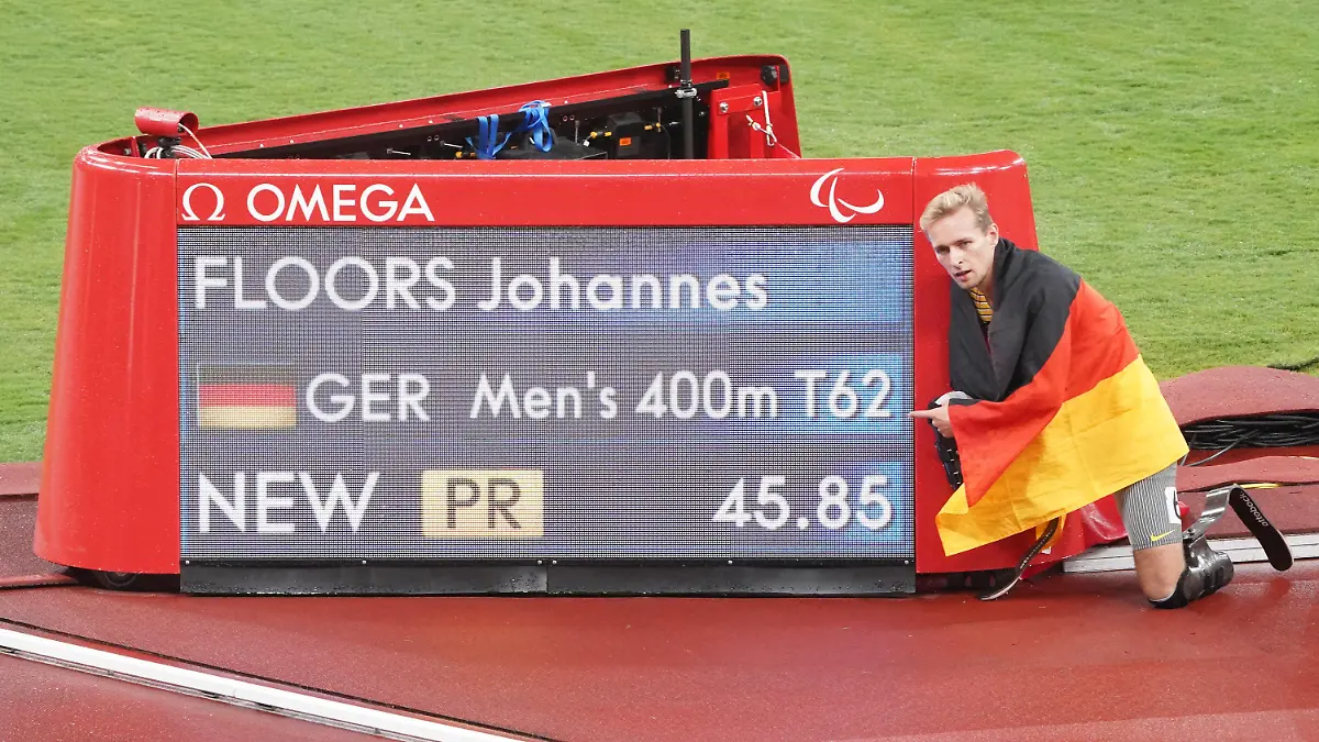 03.09.2021, Japan, Tokio: Paralympics: Leichtathletik, 400 Meter Männer, T62 Finale, im Olympiastadion. Goldmedaillen-Gewinner Johannes Floors aus Deutschland kniet nach seinem Sieg und neuem Weltrekord mit einer Deutschlandfahne auf den Schultern neben den Anzeigetafel. Foto: Marcus Brandt/dpa +++ dpa-Bildfunk +++
