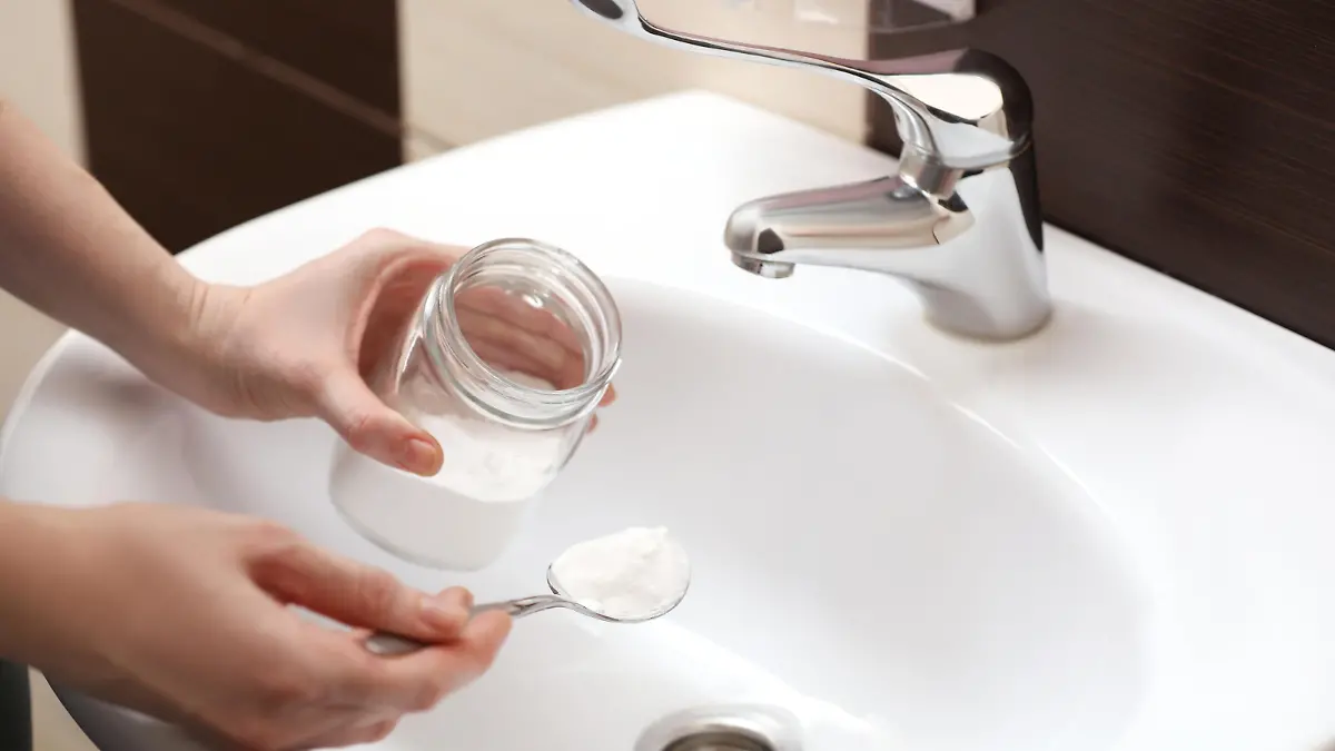 Woman using baking soda to unclog sink drain in bathroom, closeup