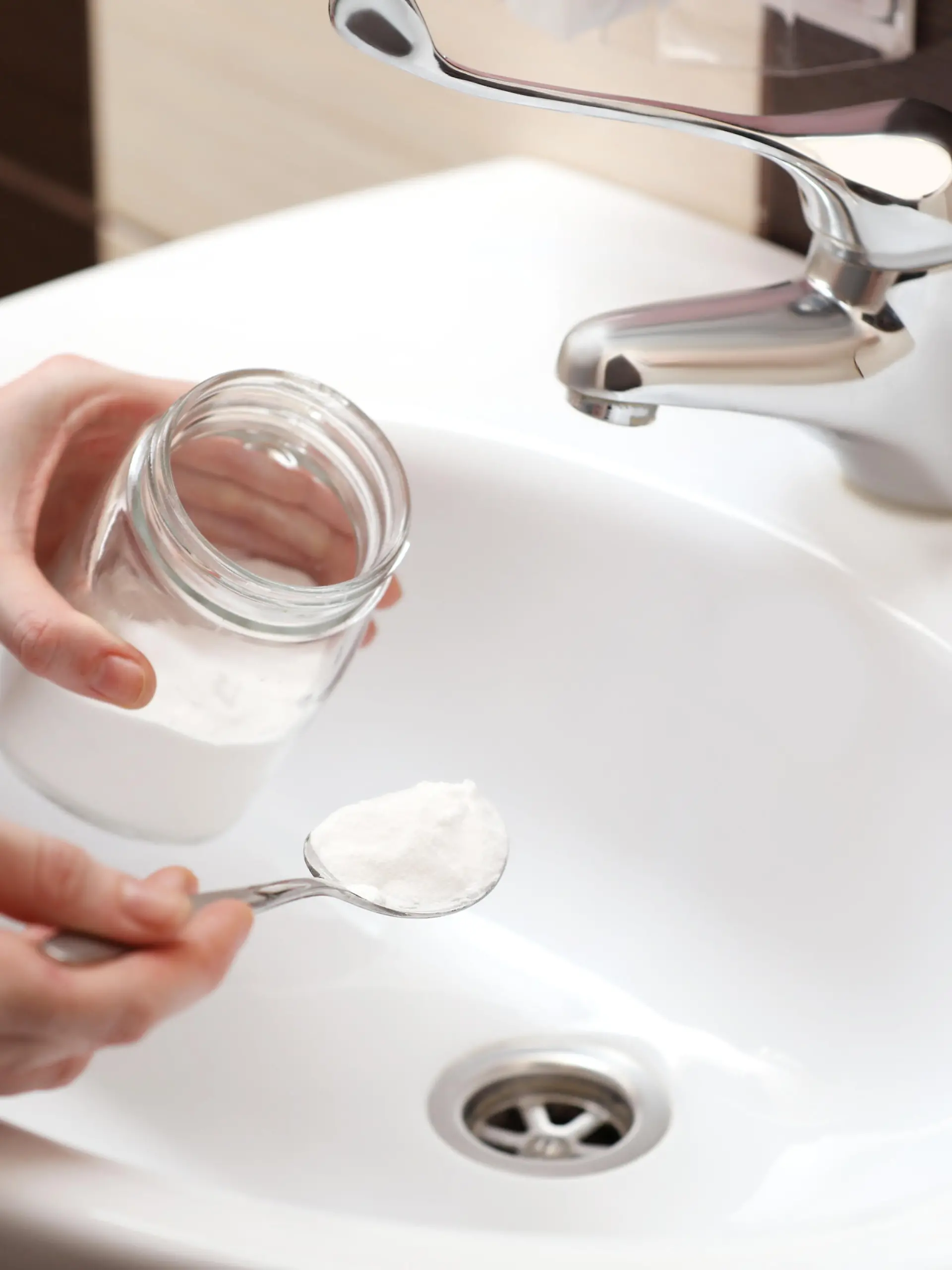 Woman using baking soda to unclog sink drain in bathroom, closeup