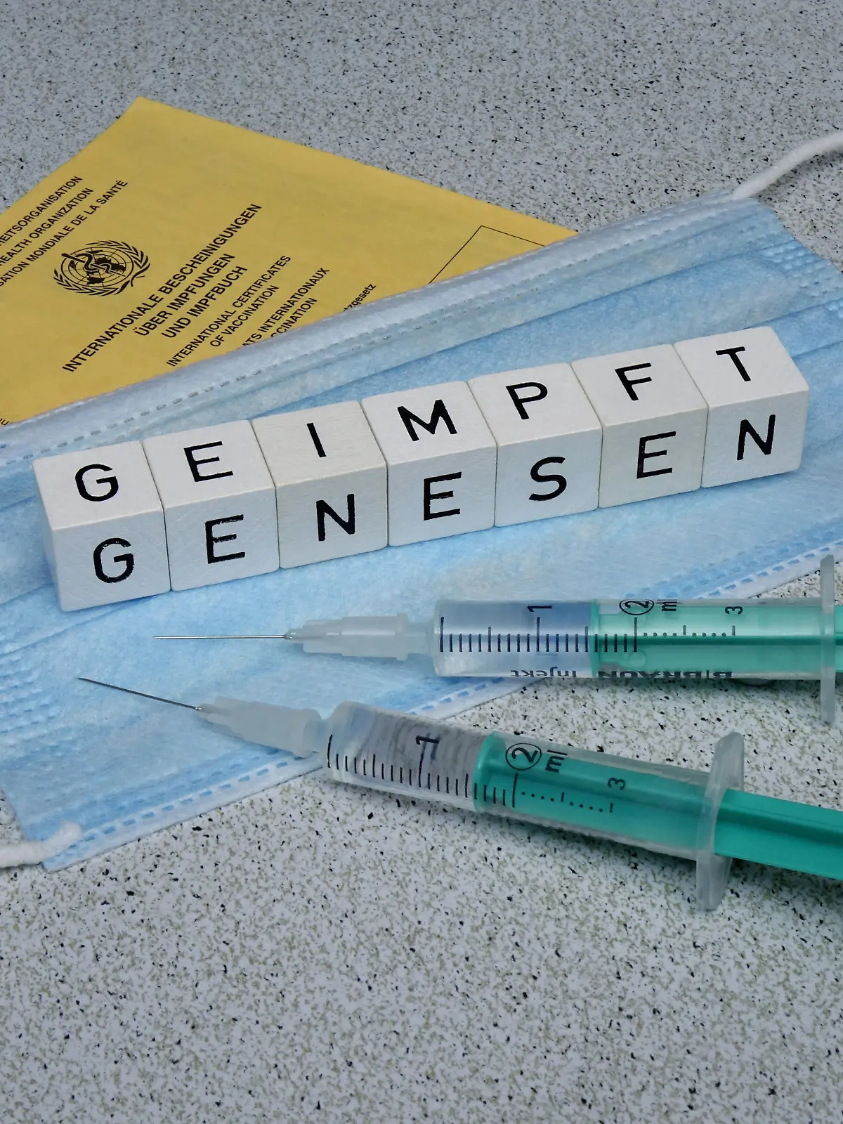 24.08.2021, Borkwalde, Brandenburg, Auf einer Mundschutzmaske liegen Buchstabenwuerfel mit den Worten geimpft und genesen.