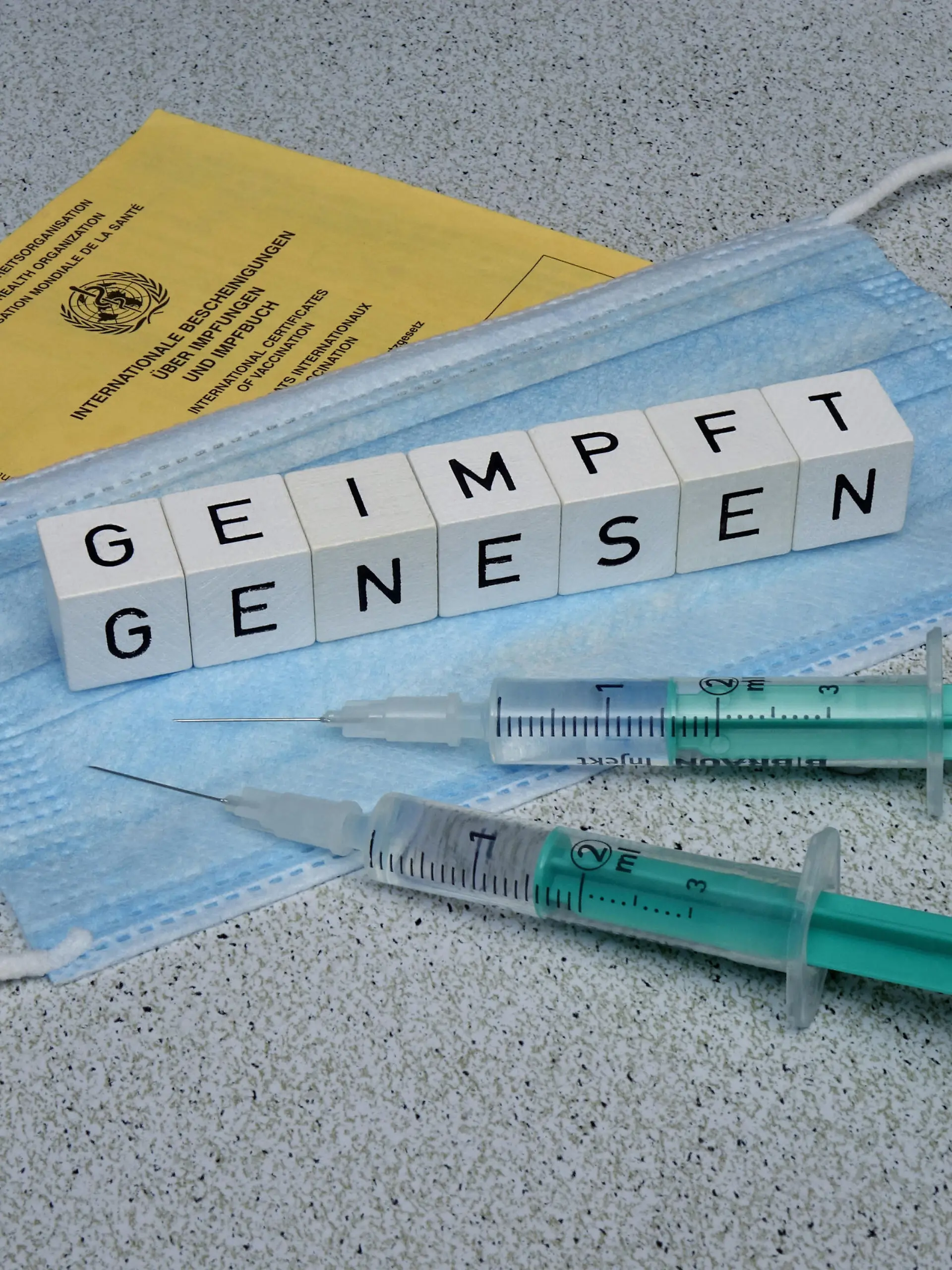 24.08.2021, Borkwalde, Brandenburg, Auf einer Mundschutzmaske liegen Buchstabenwuerfel mit den Worten geimpft und genesen.