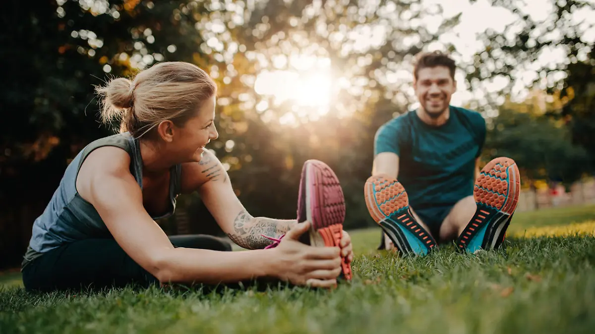 Fitness couple stretching outdoors in park. Young man and woman exercising together in morning.