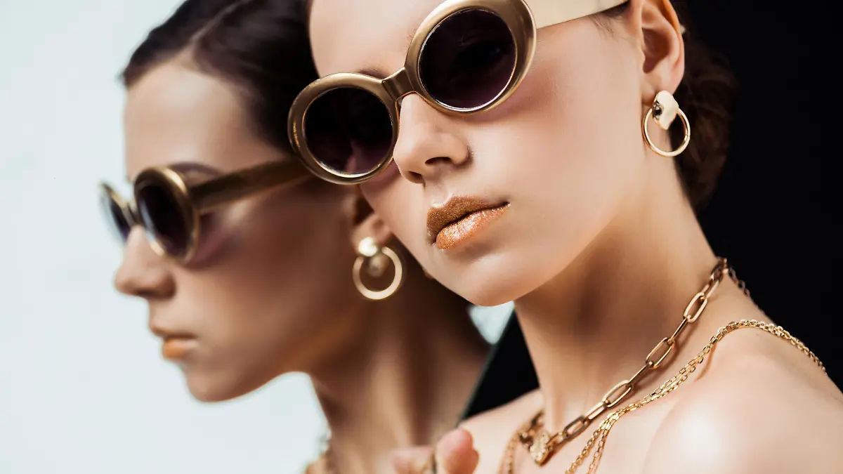 young nude woman in sunglasses, golden jewelry holding mirror isolated on black