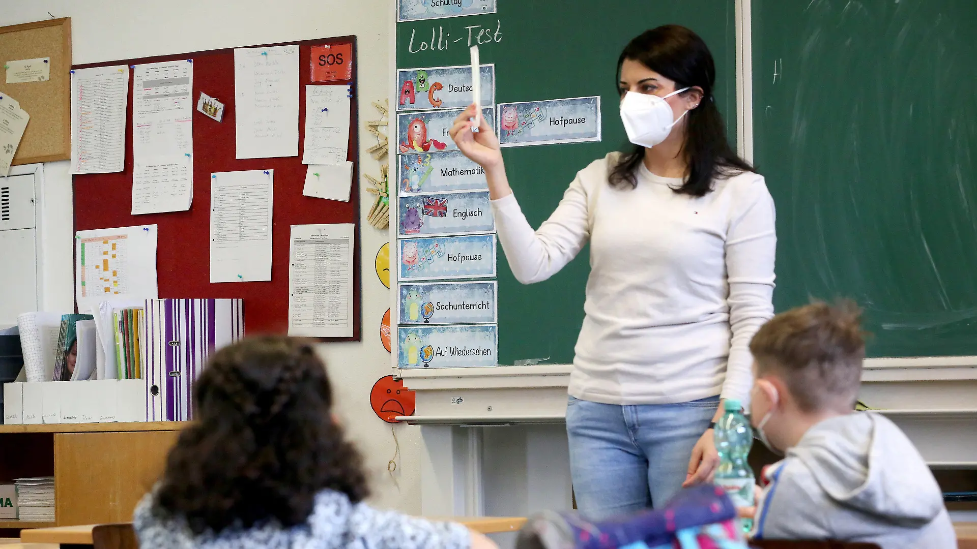 10.05.2021, Nordrhein-Westfalen, Essen: Kamuran Turan, Lehrerin der Klaase 3a der Maria-Kunigunda-Grundschule erklärt ihren Schülern den "Lolli-Test. Nordrhein-Westfalen führt am Montag sogenannte Lolli-Tests flächendeckend an allen Grund- und Förderschulen ein. Mit dem Test sollen alle mehr als 730 000 Schülerinnen und Schüler der knapp 3800 Grund- und Förderschulen zwei Mal pro Woche in ihrer jeweiligen Lerngruppe auf das Coronavirus getestet werden. Foto: Roland Weihrauch/dpa - ACHTUNG: Nur zur redaktionellen Verwendung im Zusammenhang mit der aktuellen Berichterstattung über die Einführung der Tests in den Schulen in NRW. +++ dpa-Bildfunk +++