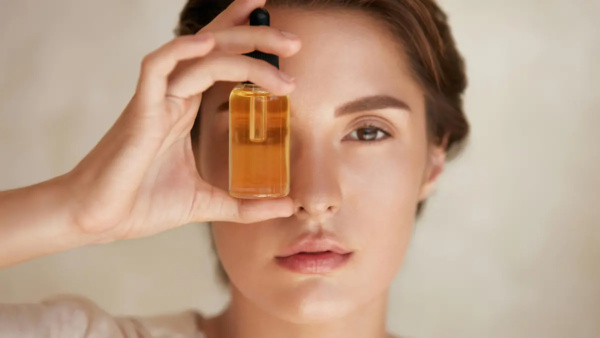 Beauty Face. Close Up Portrait Of Woman With Bottle Of Essential Oil. Beautiful Model With Radiant And Glowing Facial Skin Looking At Camera. Moisturizing With Serum Collagen And Hyaluronic Acid.