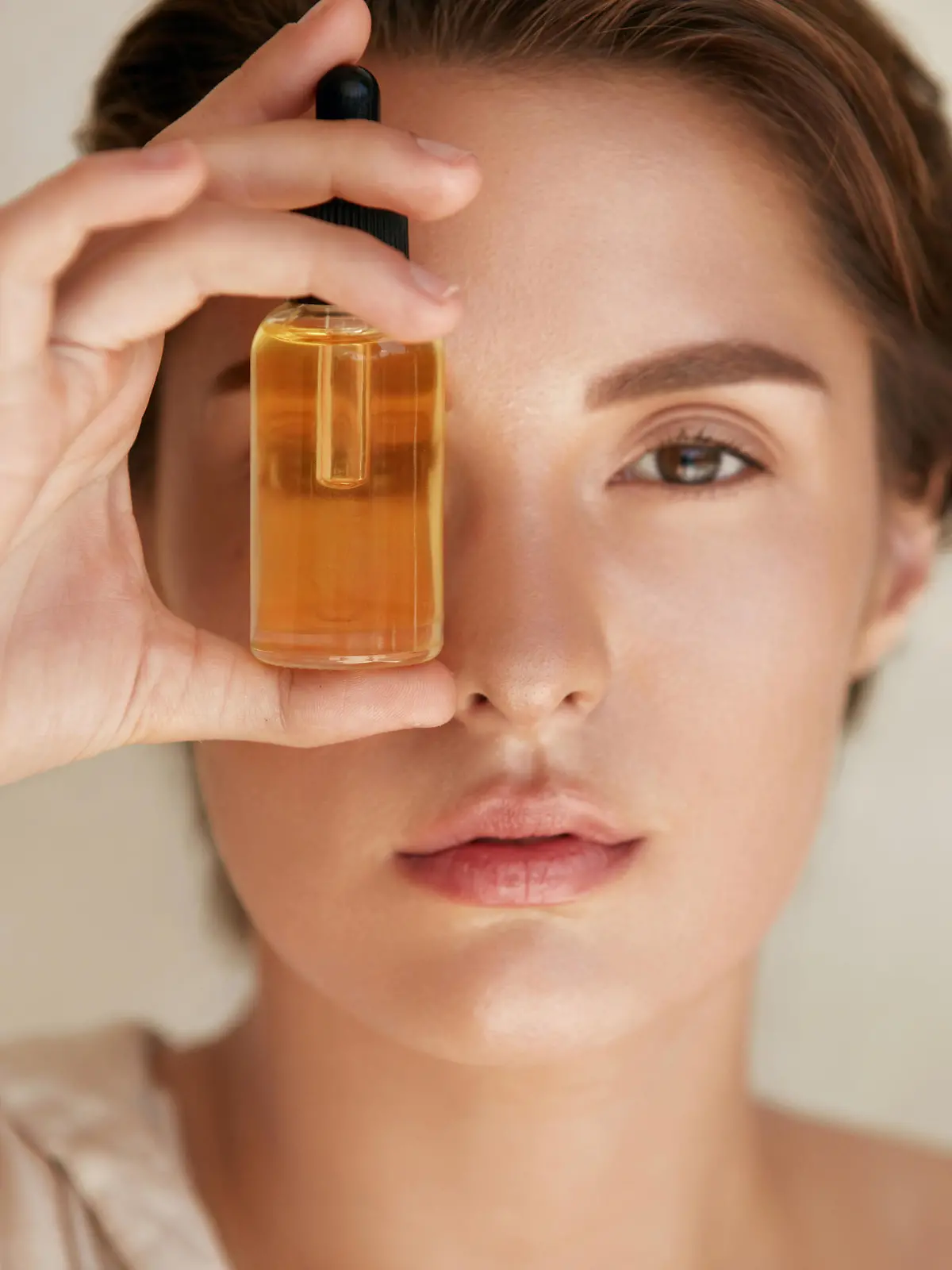 Beauty Face. Close Up Portrait Of Woman With Bottle Of Essential Oil. Beautiful Model With Radiant And Glowing Facial Skin Looking At Camera. Moisturizing With Serum Collagen And Hyaluronic Acid.
