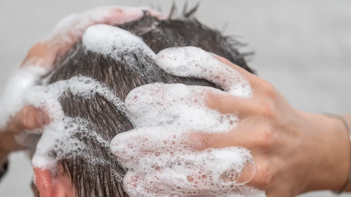 Ein junger Mann duscht. Zu sehen ist sein Kopf, der mit Shampoo gewaschen wird.