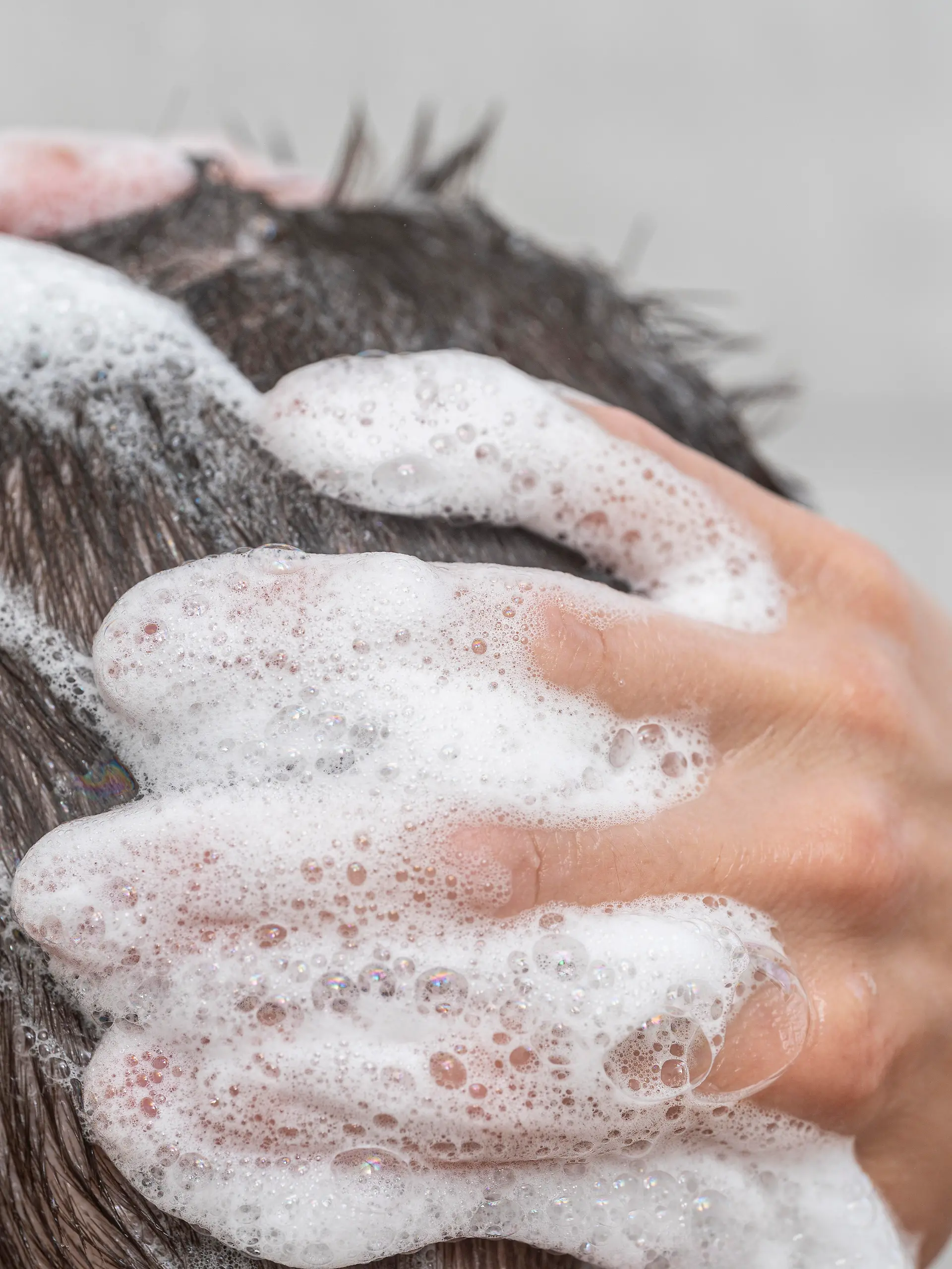 Ein junger Mann duscht. Zu sehen ist sein Kopf, der mit Shampoo gewaschen wird. 