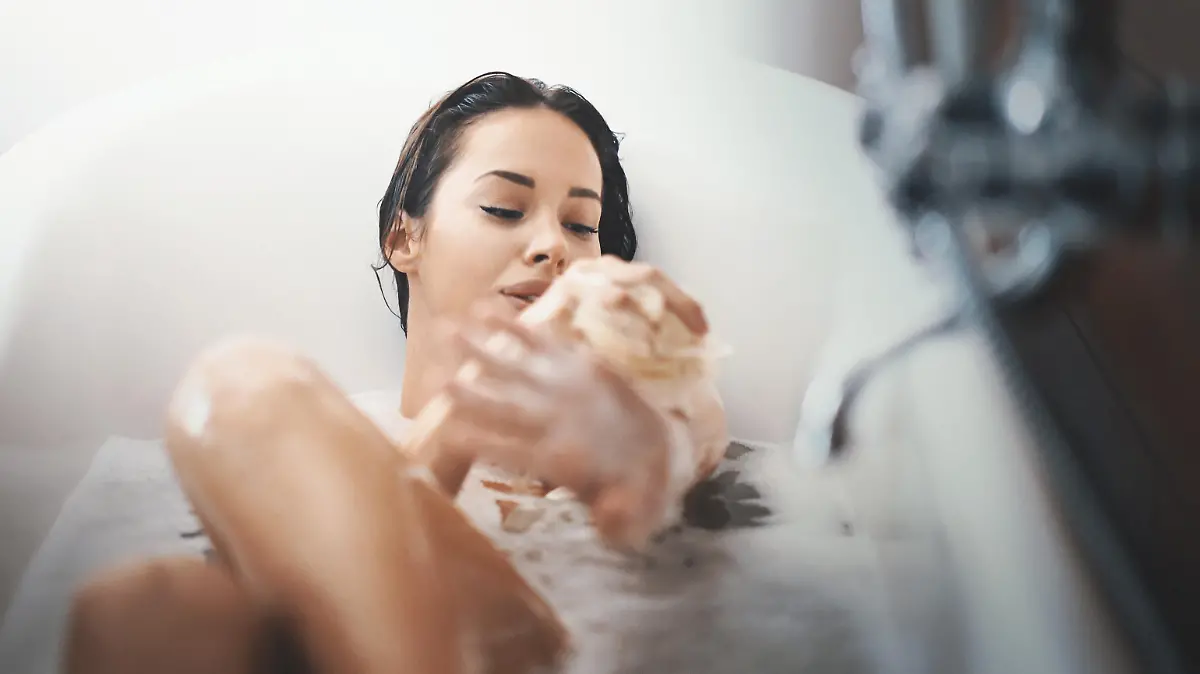 Closeup of attractive mid 20's woman taking a long bath in a bathtub. She's slowly scrubbing off with a bath sponge and not planning to get out some time soon.