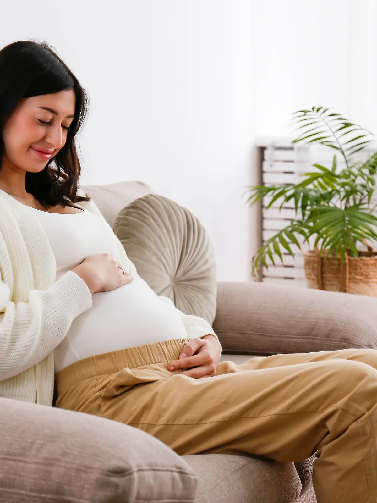 Young beautiful pregnant woman on second trimester of pregnancy sitting on the couch of doctor's office waiting for checkup. Regular prenatal care visit concept. Background, copy space, close up