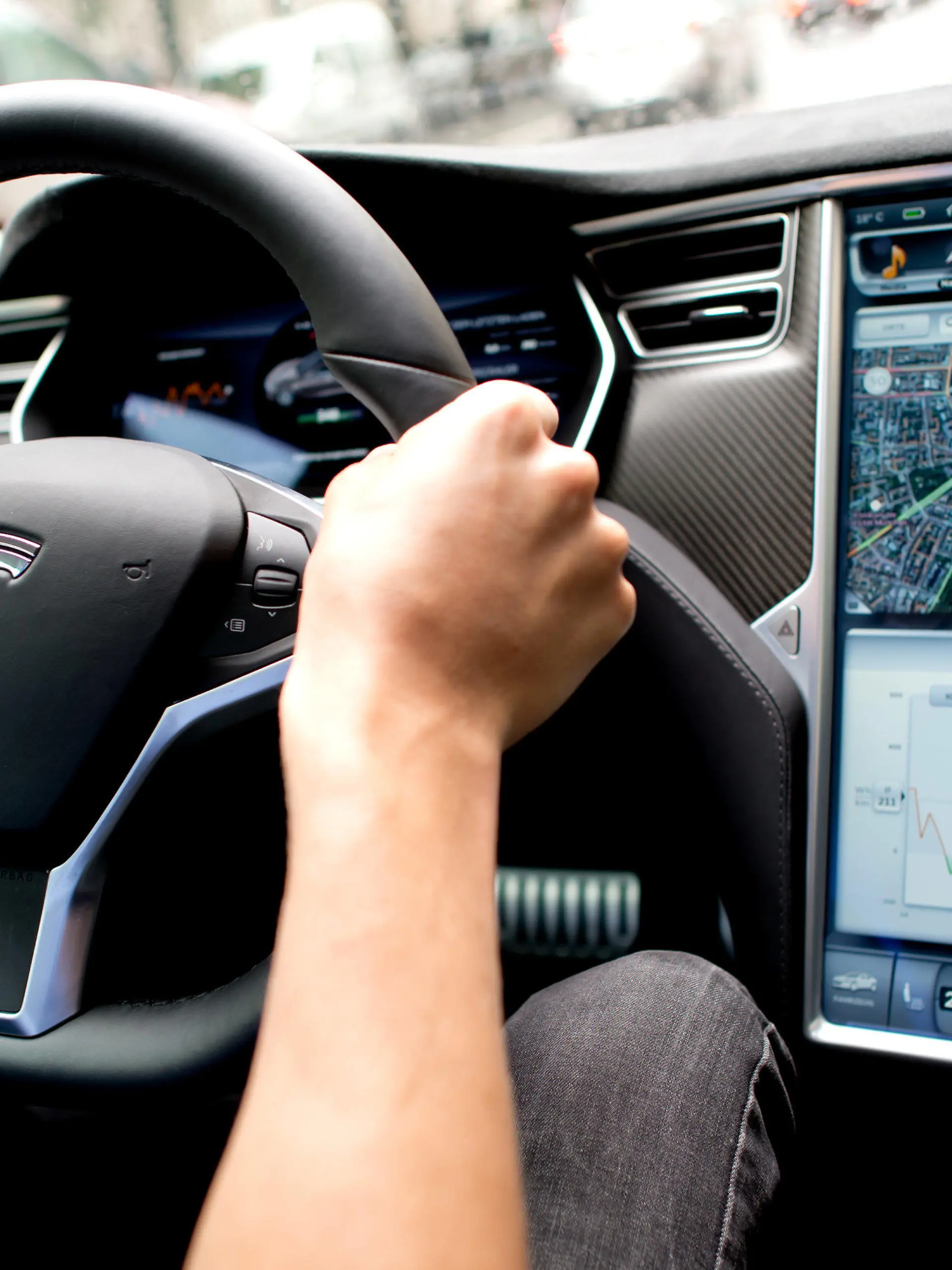 ARCHIV - 17.08.2015, Bayern, München: Ein Mann sitzt in einem Tesla Model S am Lenkrad, neben ihm ein großer Monitor im Armaturenbrett.   
(zu dpa "Behörde prüft Fehlfunktion von Tesla-Bildschirm") Foto: picture alliance / dpa +++ dpa-Bildfunk +++