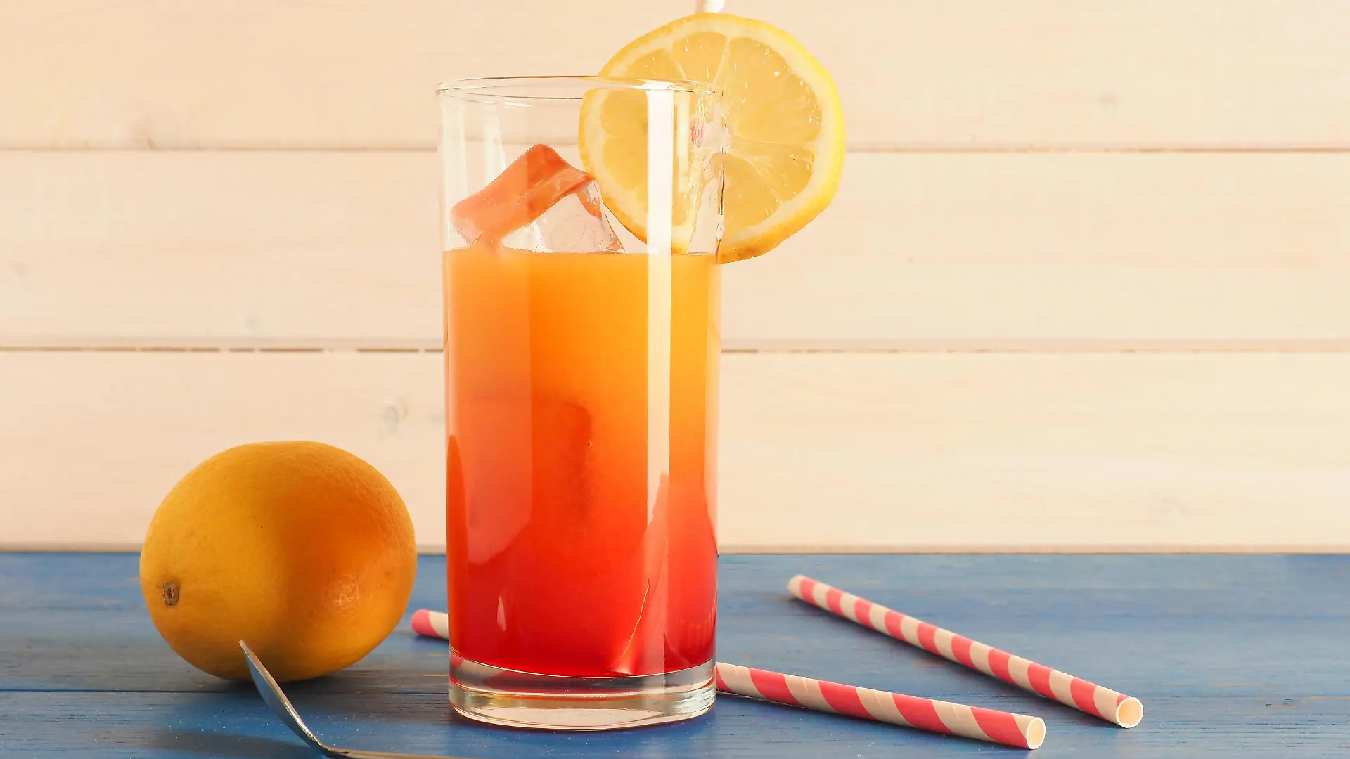 Non alcoholic cocktail with orange and lemon juice and grendine syrup on ice, tasty summer drink on a wooden background