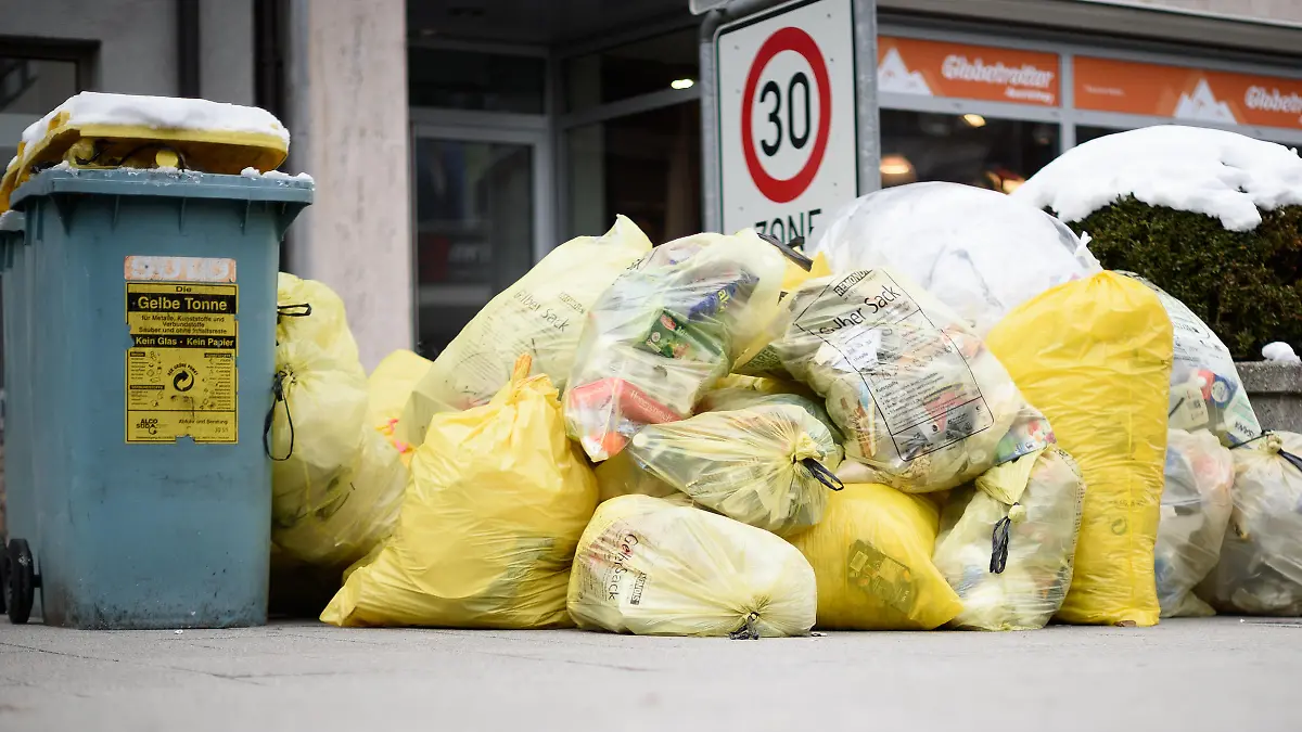 22.02.2018, Baden-Württemberg, Ulm: Mülltonnen und gelbe Säcke mit Kunststoff-Abfällen (Grüner Punkt) stapeln sich auf einem Fußweg. Foto: Sina Schuldt/dpa