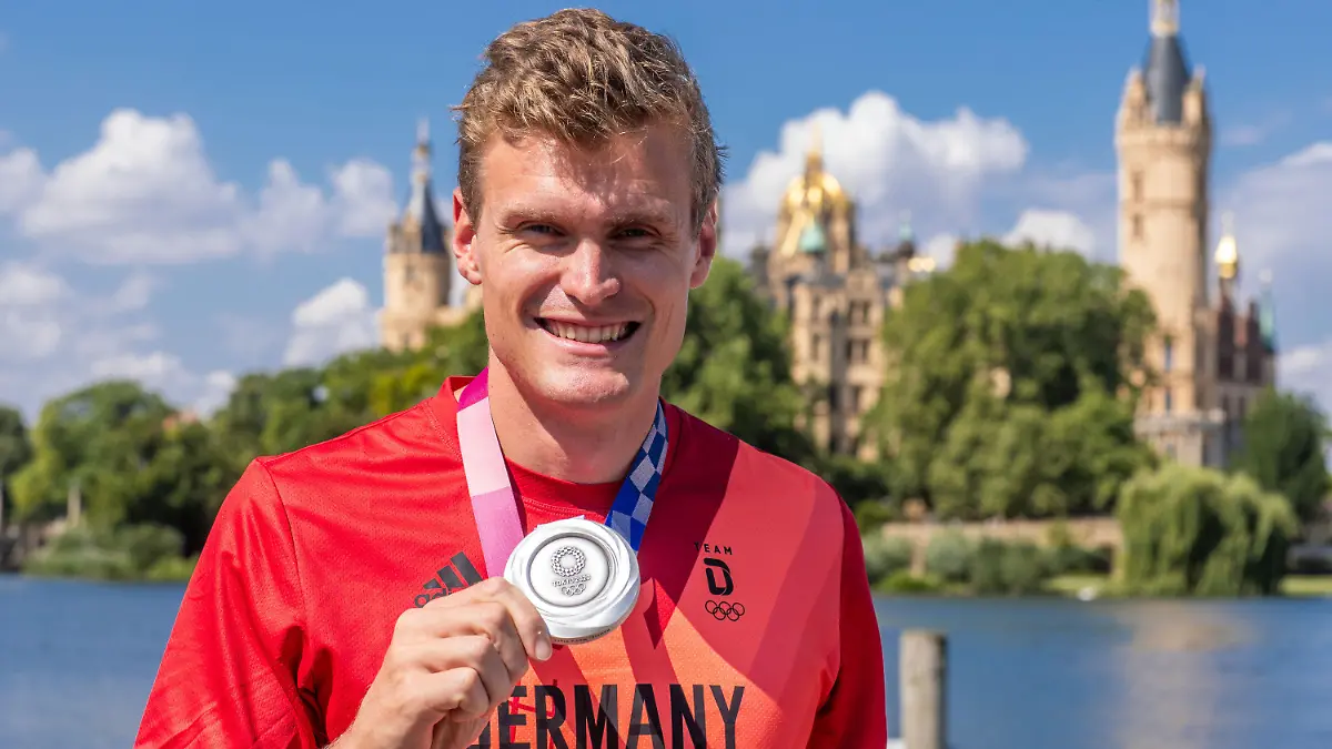 06.08.2021, Mecklenburg-Vorpommern, Schwerin: Hannes Ocik, Schlagmann im deutschen Ruderachter bei den Olympischen Spielen in Tokio, steht mit seiner Silbermedaille beim Empfang vor dem Schweriner Schloß. Ocik wurde im Ruderverein Schwerin nach seiner Rückkehr aus Japan begrüßt. Foto: Jens Büttner/dpa-Zentralbild/dpa +++ dpa-Bildfunk +++