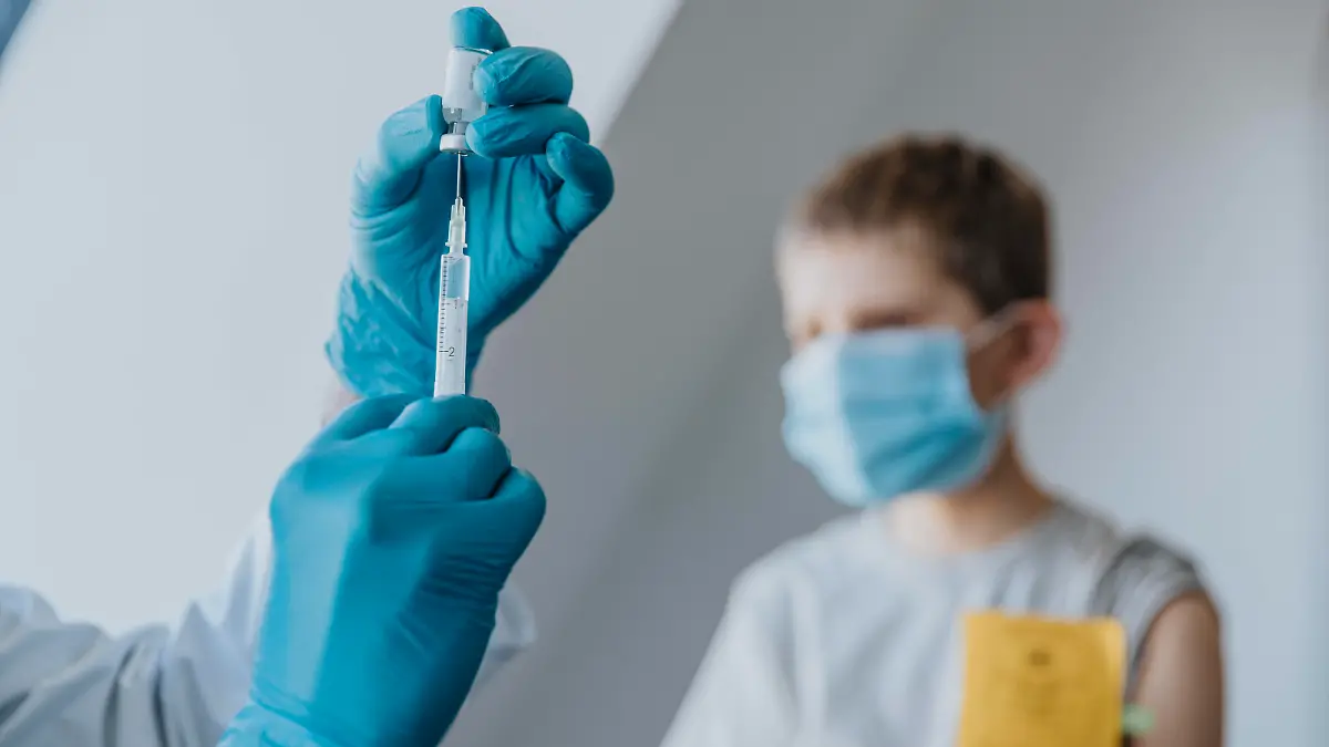 Doctor filling syringe with COVID-19 vaccine for boy in background at clinic model released Symbolfoto property released MFF07482 