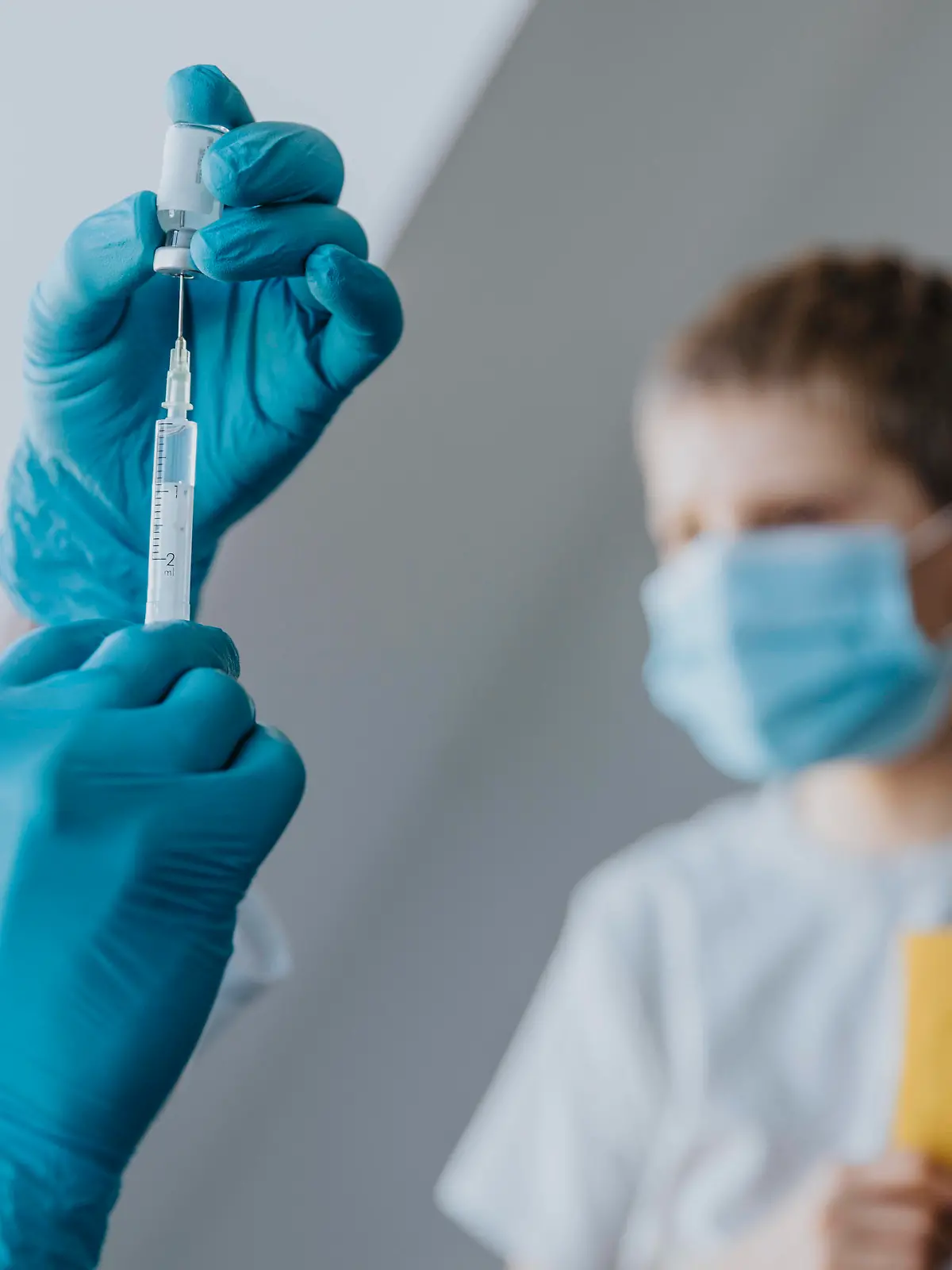Doctor filling syringe with COVID-19 vaccine for boy in background at clinic model released Symbolfoto property released MFF07482 