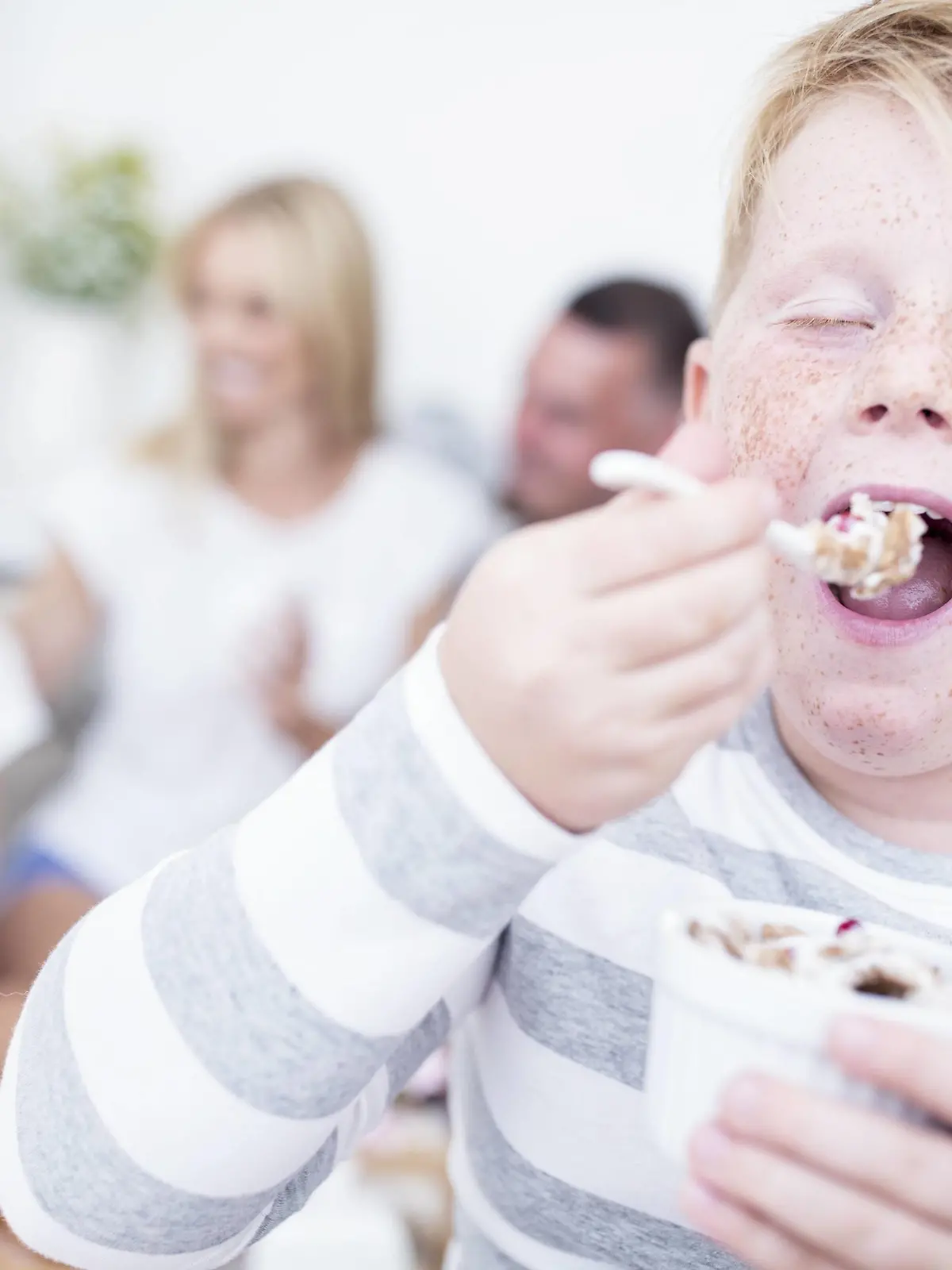 Boy eating from cereal bowl with family in background model released Symbolfoto property released PUBLICATIONxINxGERxSUIxAUTxHUNxONLY WESTF22570  