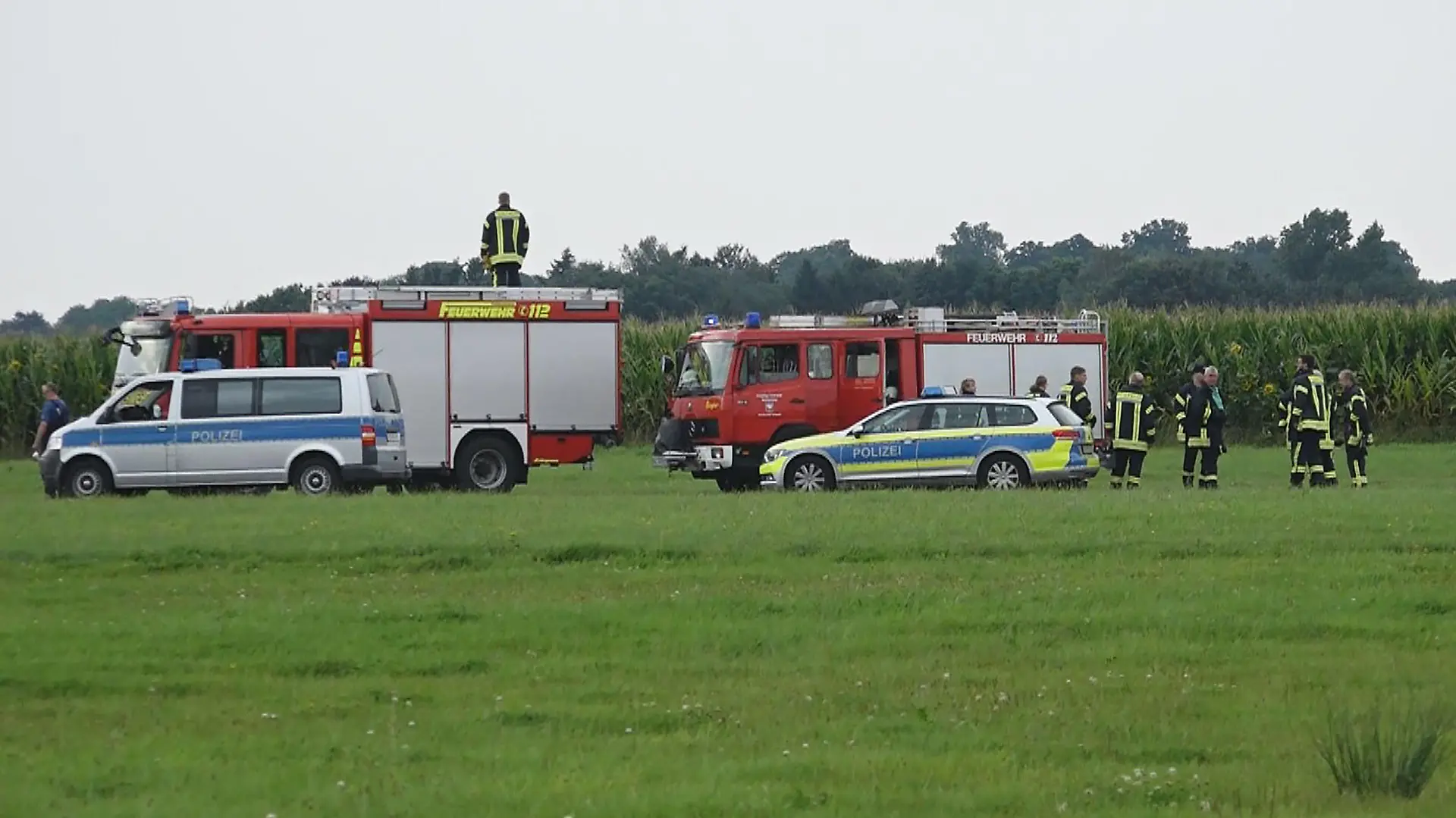 22.08.2021, Niedersachsen, Ganderkesee: Feuerwehrleute und Polizisten stehen am Rande eines Maisfeldes in dem ein tödlich verunglückter Fallschirmspringer gefunden wurde. (zu dpa "35-Jähriger kommt bei Fallschirmsprung ums Leben") Foto: Nonstop News/dpa +++ dpa-Bildfunk +++