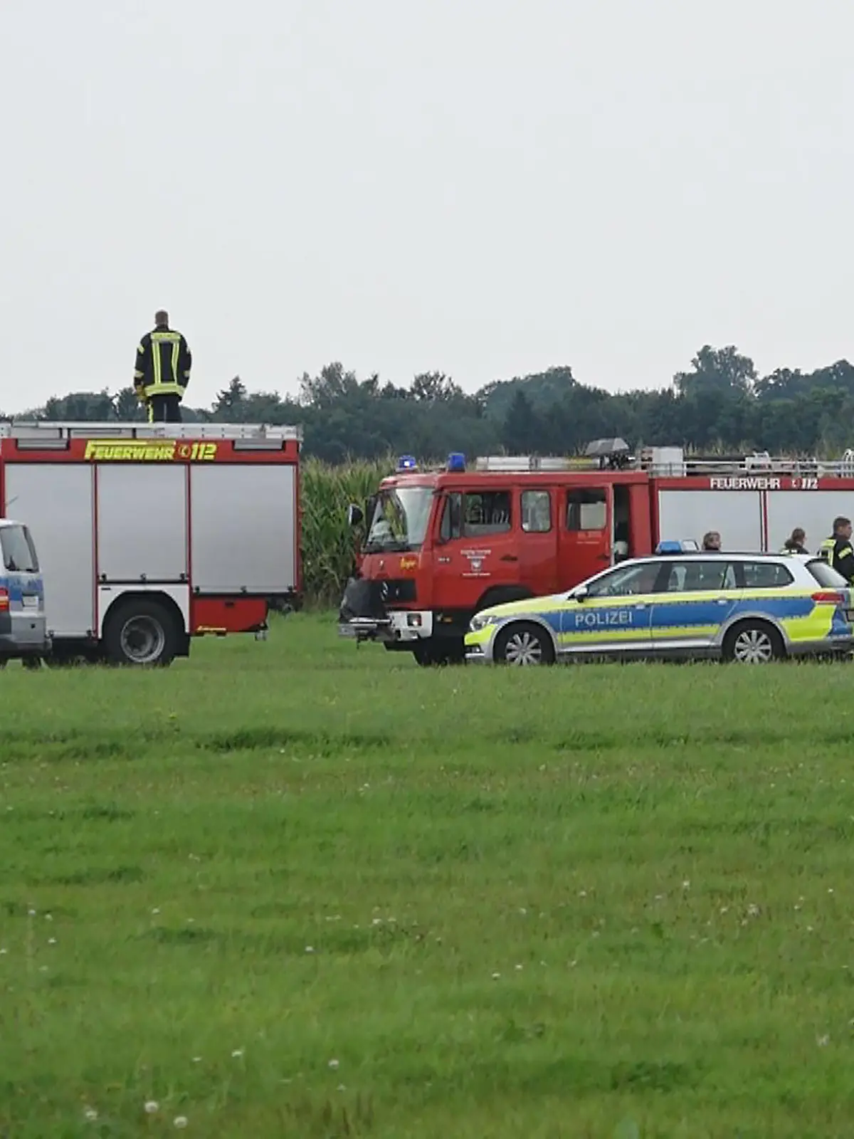 22.08.2021, Niedersachsen, Ganderkesee: Feuerwehrleute und Polizisten stehen am Rande eines Maisfeldes in dem ein tödlich verunglückter Fallschirmspringer gefunden wurde.    (zu dpa "35-Jähriger kommt bei Fallschirmsprung ums Leben") Foto: Nonstop News/dpa +++ dpa-Bildfunk +++