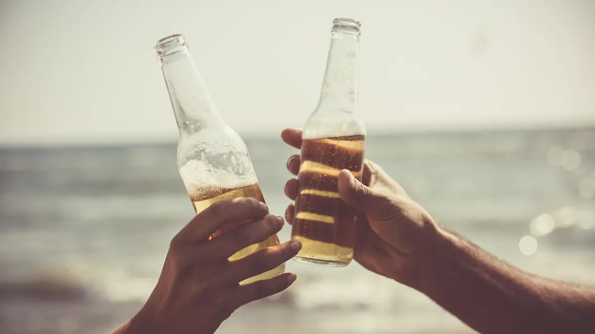 Close-up shot of male and female hand doing celebratory toast with beer bottles at the beach.