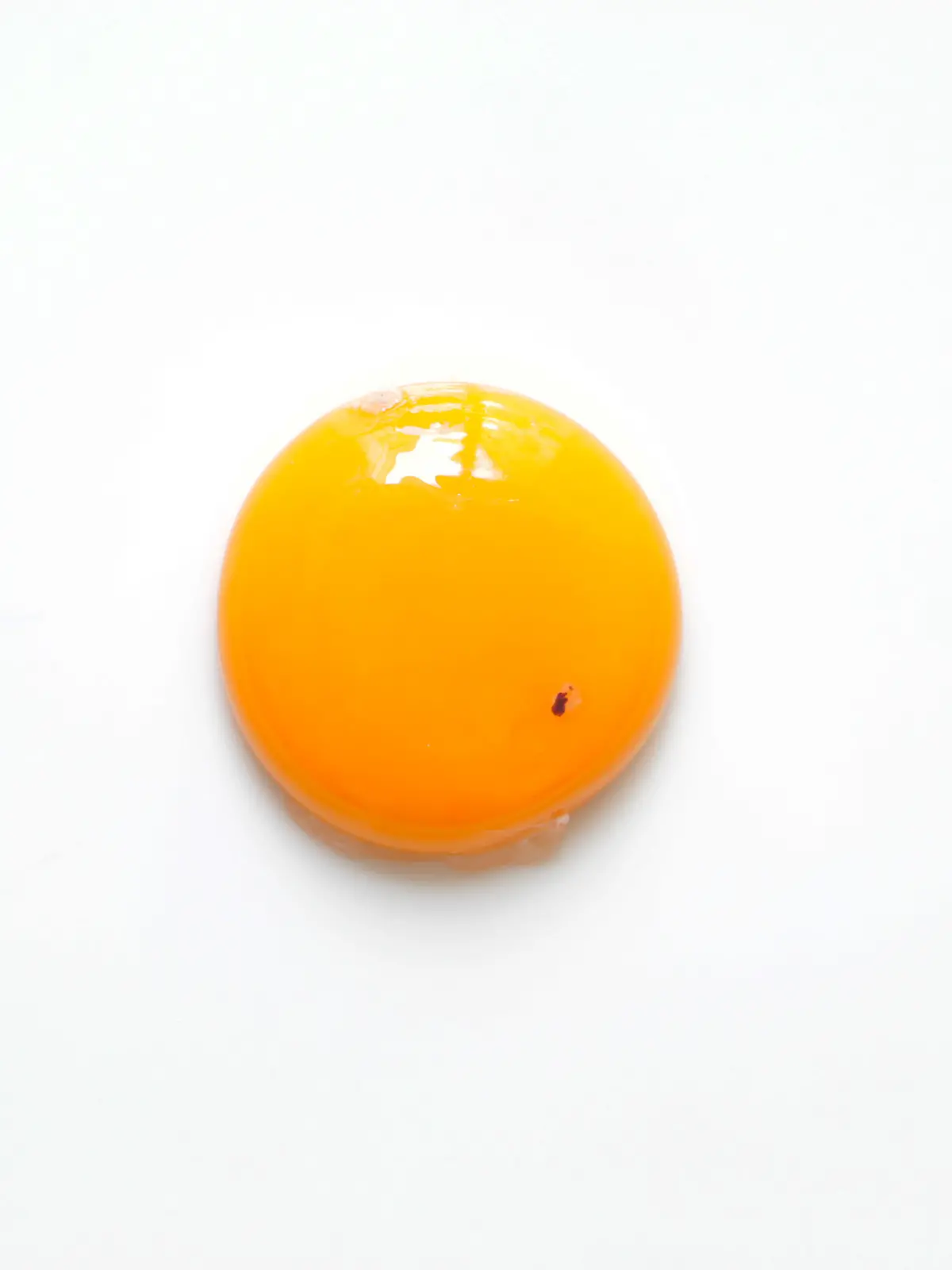 Raw chicken egg yolk with blood spot, flat lay on white background