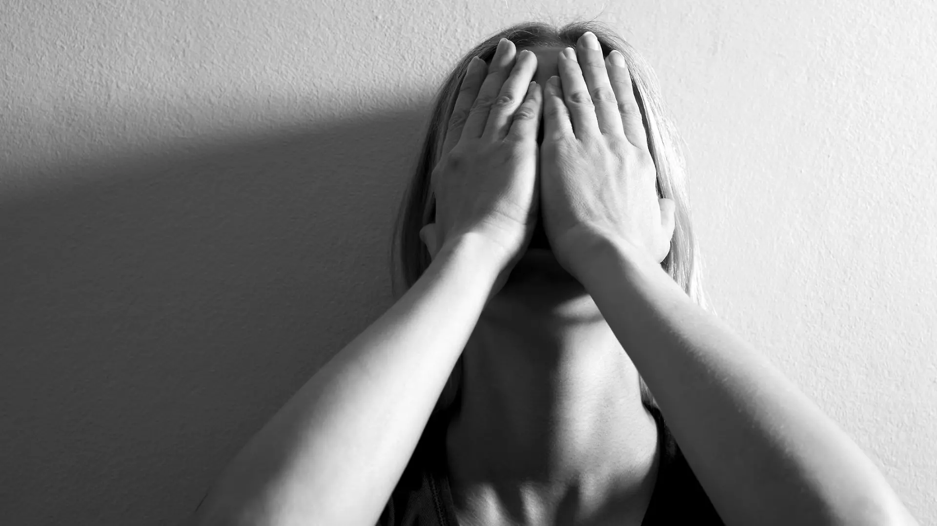 Woman with hands on her face leaning on wall