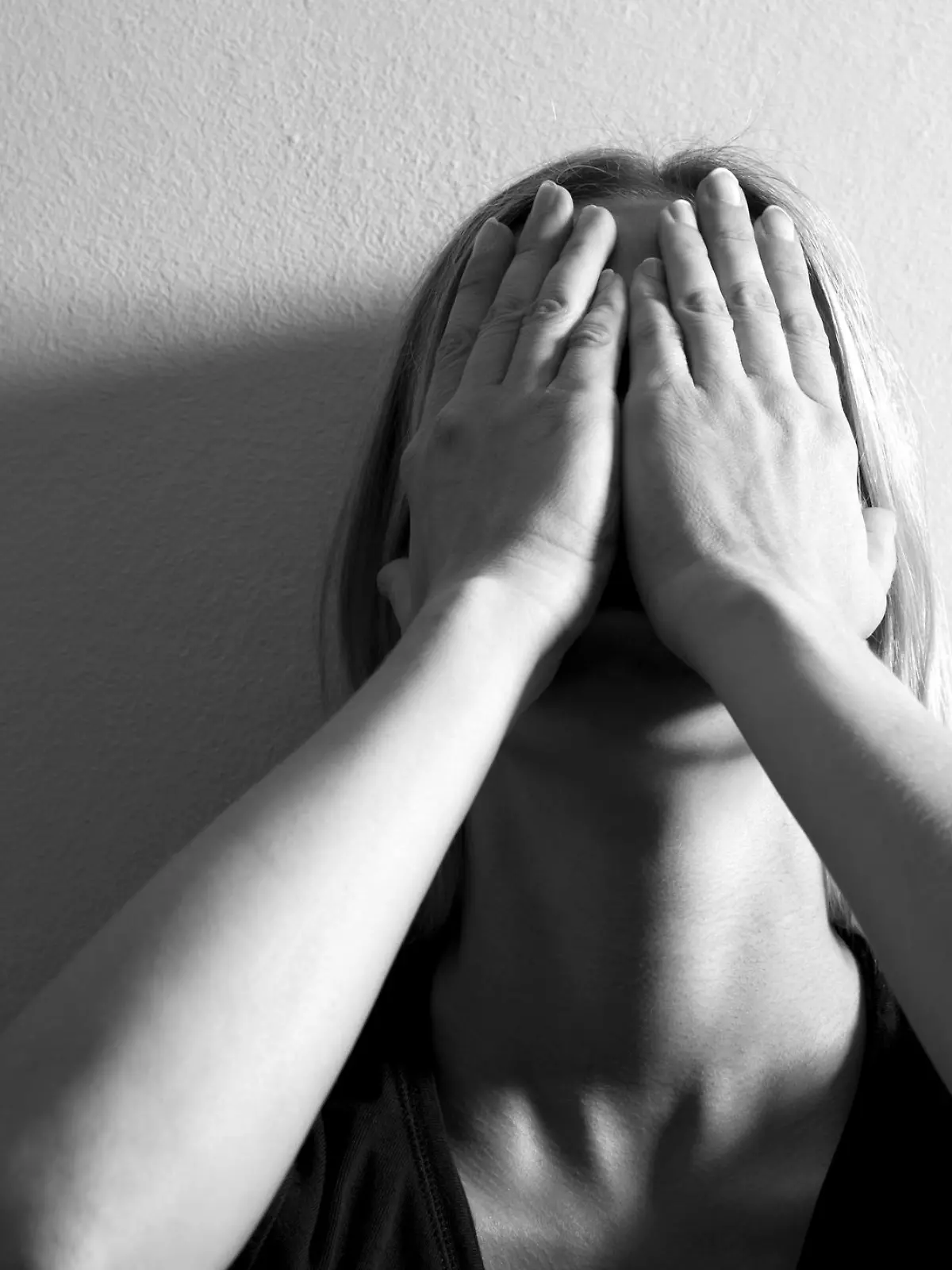 Woman with hands on her face leaning on wall