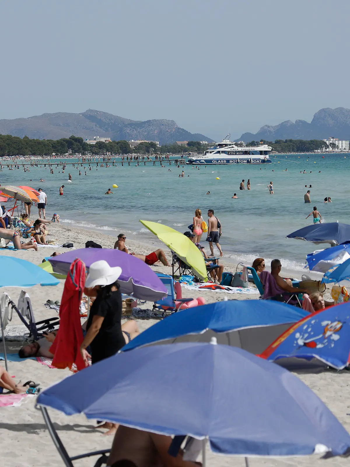 11.07.2021, Spanien, -: Unter bunten Sonnenschirmen genießen viele Menschen Sonne, Sand und Meer am Strand von Playa de Muro im Norden von Mallorca. Die Bundesregierung hat ganz Spanien mit Mallorca und den Kanaren angesichts rapide ansteigender Corona-Zahlen zum Risikogebiet erklärt. Die praktischen Auswirkungen für Mallorca-Urlauber halten sich zunächst aber in Grenzen. Foto: Clara Margais/dpa +++ dpa-Bildfunk +++