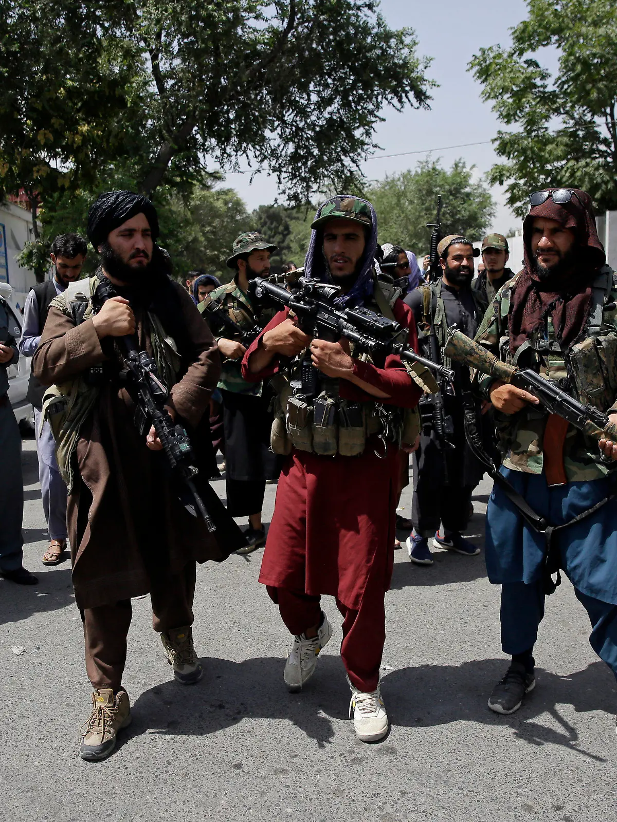 19.08.2021, Afghanistan, Kabul: Schwer bewaffnete Taliban-Kämpfer patrouillieren vor zwei Verkehrspolizisten (l). Foto: Rahmat Gul/AP/dpa +++ dpa-Bildfunk +++