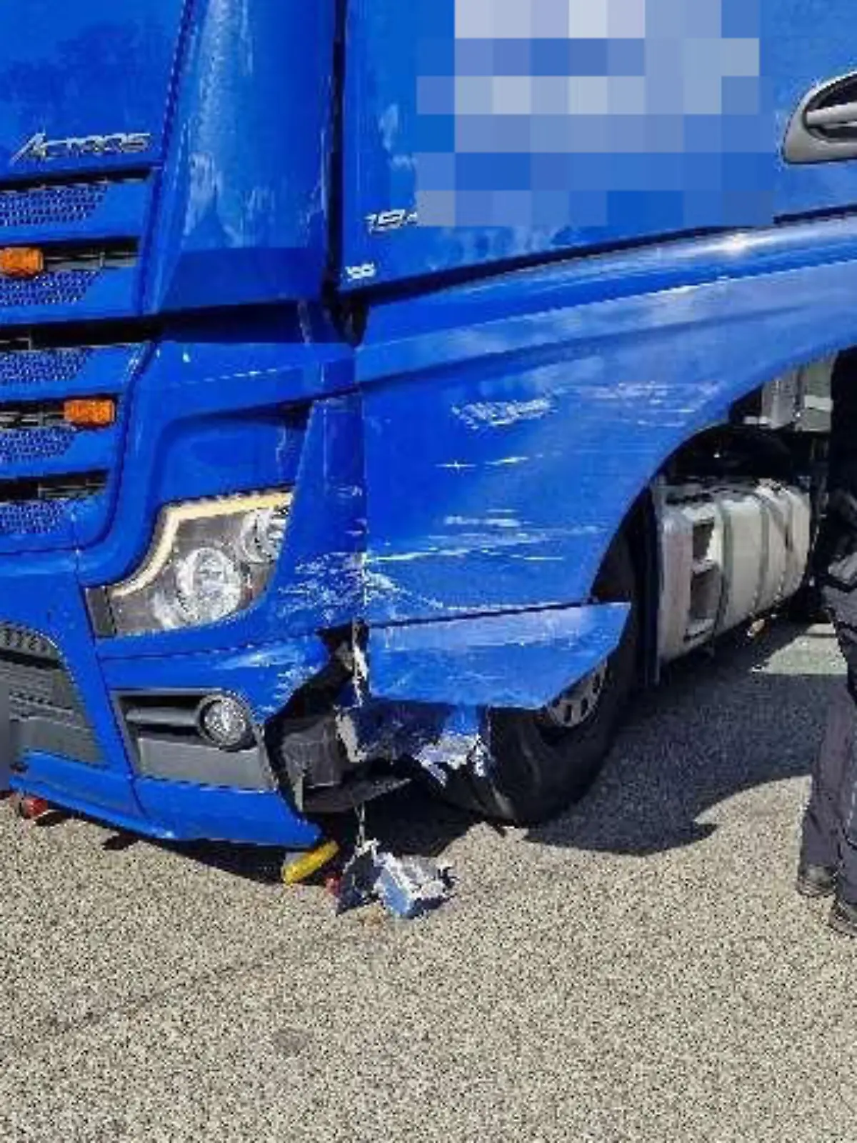 Ein blauer LKW steht auf einer Kreuzung, im Lack sind Kratzspuren zu erkennen.