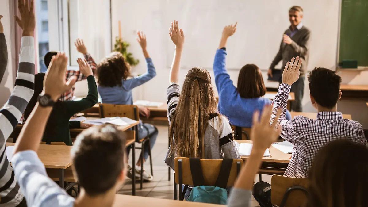 Rear view of large group of students raising their hands to answer the question on a class.