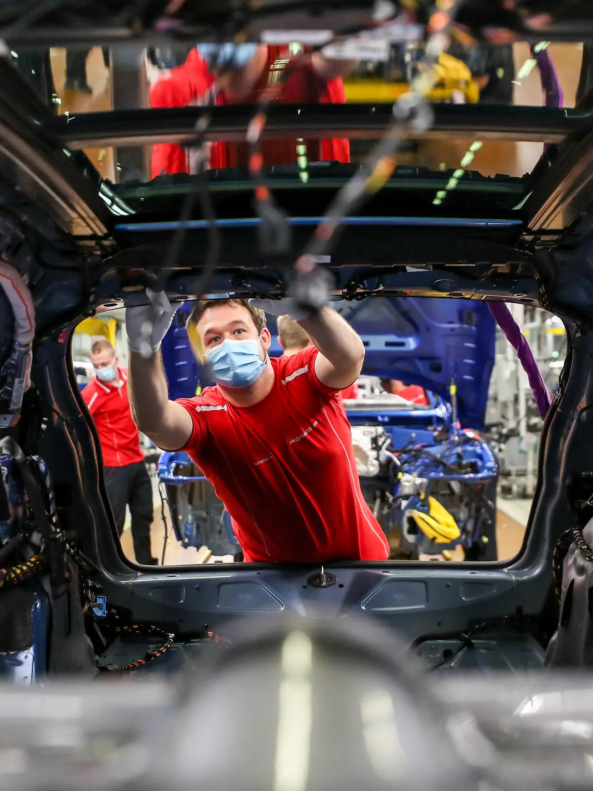 ARCHIV - 07.05.2020, Sachsen, Leipzig: Ein Mitarbeiter von Porsche arbeitet mit Mundschutz in der Montage an einem Macan. Die Coronakrise hat nach Einschätzung der Organisation für wirtschaftliche Zusammenarbeit und Entwicklung (OECD) schlimmere Auswirkungen auf die Wirtschaft als die Finanzkrise 2009. Foto: Jan Woitas/dpa-Zentralbild/dpa +++ dpa-Bildfunk +++