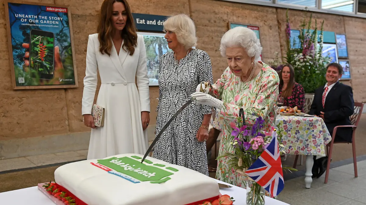 Britain's Queen Elizabeth II, centre, cuts a cake as Camilla, the Duchess of Cornwall, background centre and Kate, the Duchess of Cambridge stand by, as they attend an event in celebration of 'The Big Lunch 'initiative, during the G7 summit in Cornwall, England, Friday June 11, 2021. (Oli Scarff/Pool Photo via AP)