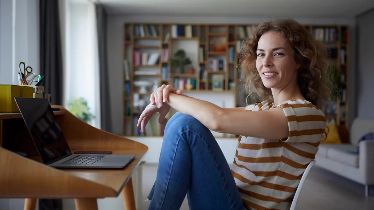 Woman smiling while sitting by desk on chair at home model released Symbolfoto property released RBF08032