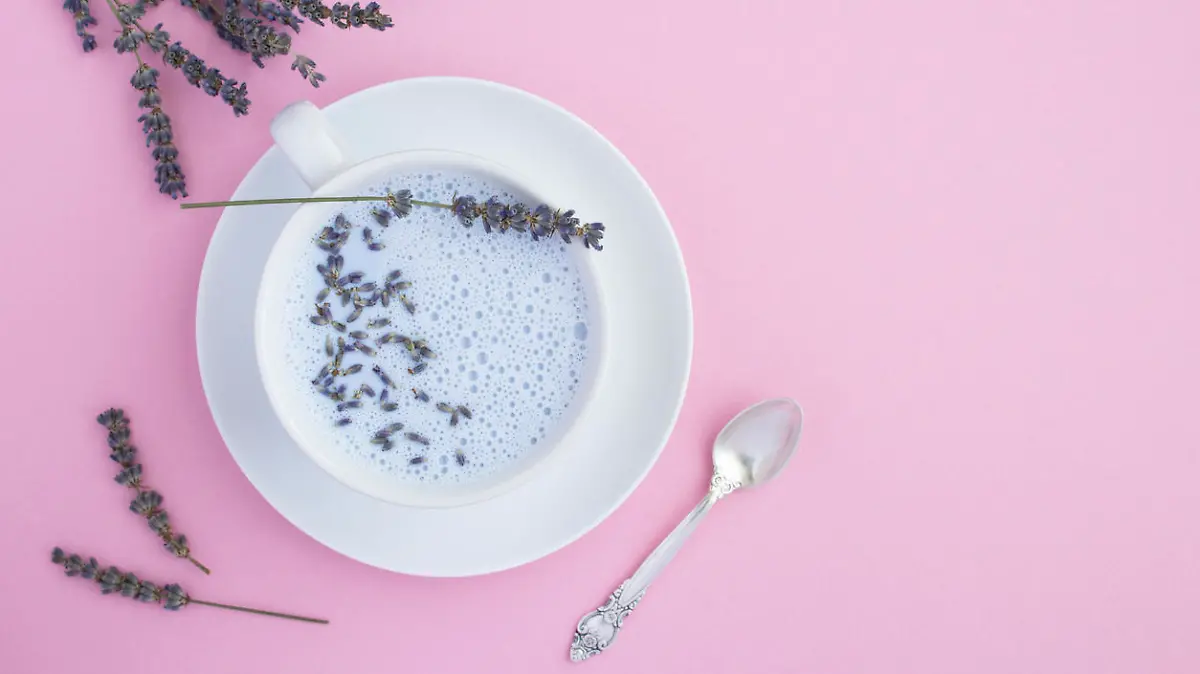 Top view of lavender moon milk in the white cup on the pink surface. Copy space.