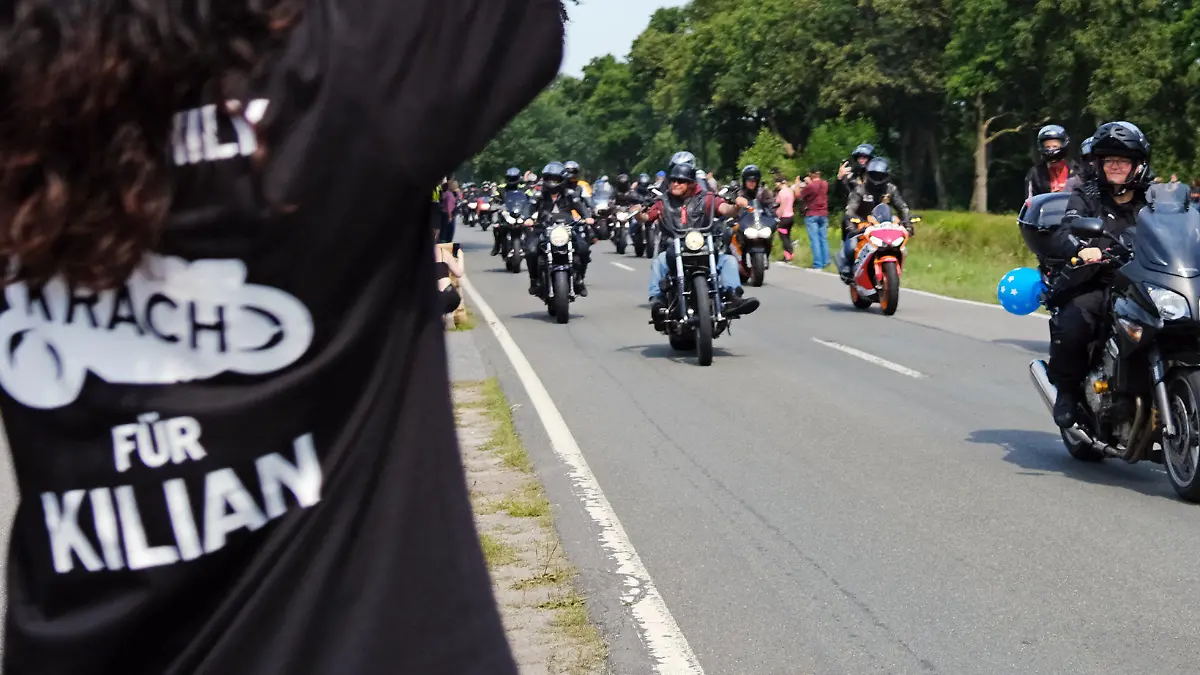 24.07.2021, Niedersachsen, Rhauderfehn: Eine Frau mit einem T-Shirt mit der Aufschrift "Krach für Kilian" winkt den Motorradfahrern, die am Haus des krebskranken Kilian vorbei fahren. Mehrere Tausend Motorradfahrer und -fahrerinnen haben sich getroffen, um dem kranken Jungen eine Freude zu machen. Das Kind ist großer Motorradfan. Foto: Markus Hibbeler/dpa +++ dpa-Bildfunk +++