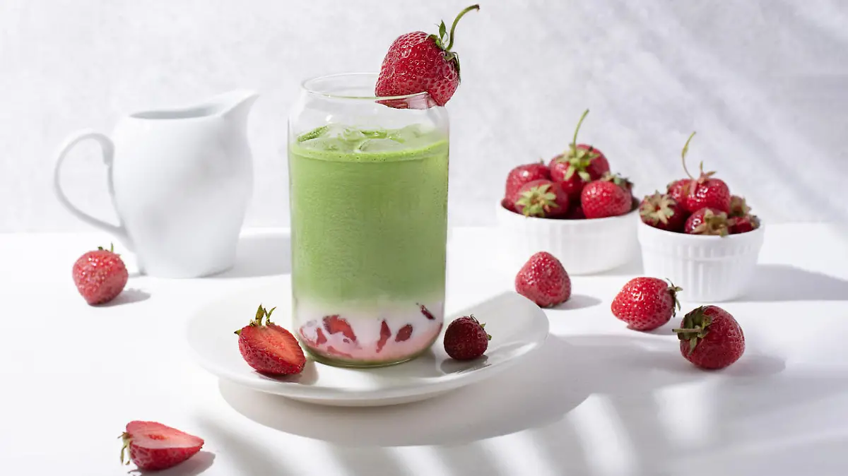 Glass with strawberry matcha latte with strawberries on a white background with beautiful shadows from the branches, close-up.