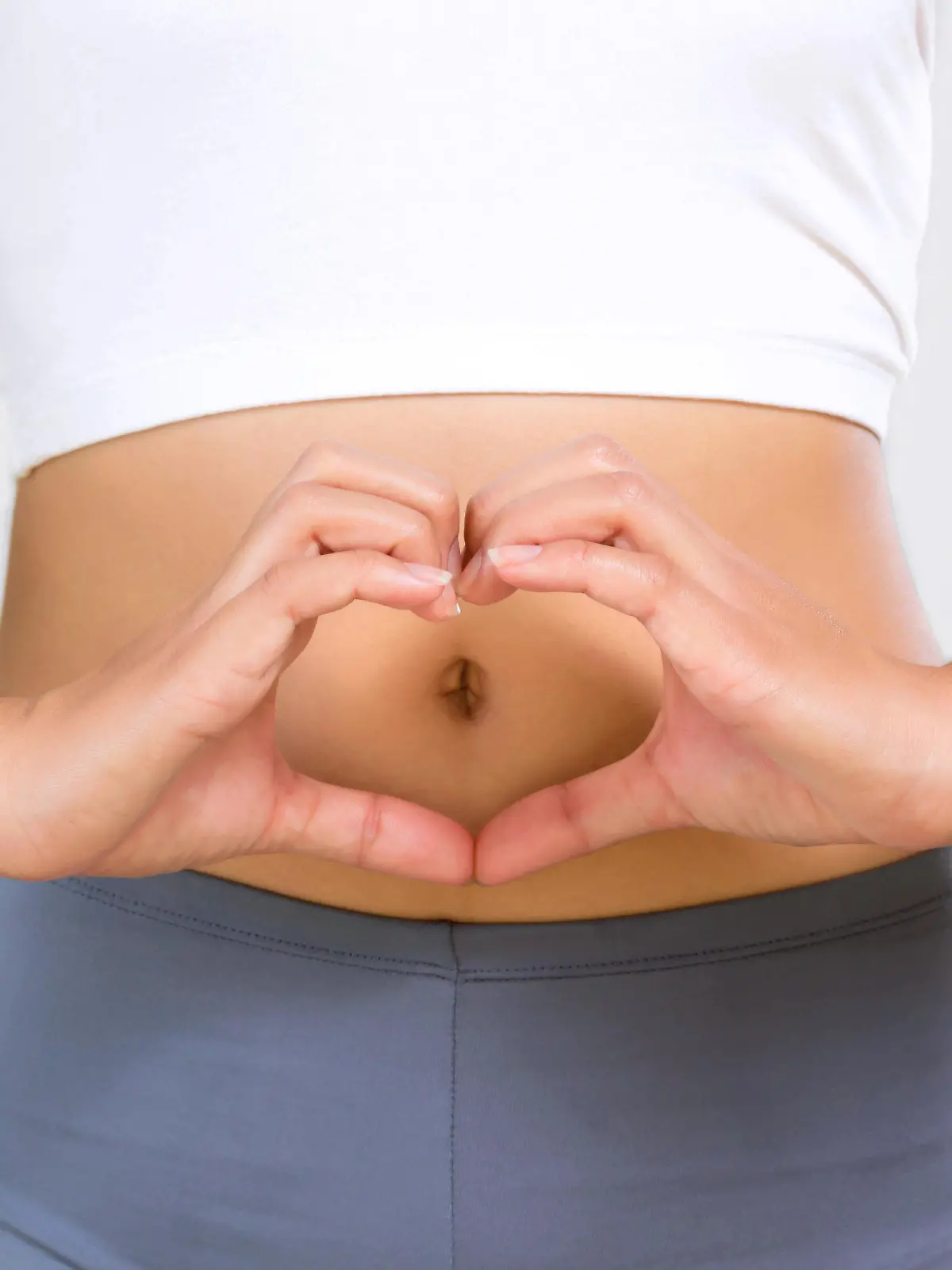 Eine schlanke Frau formt mit ihren Händen ein Herz über ihrem Bauch.