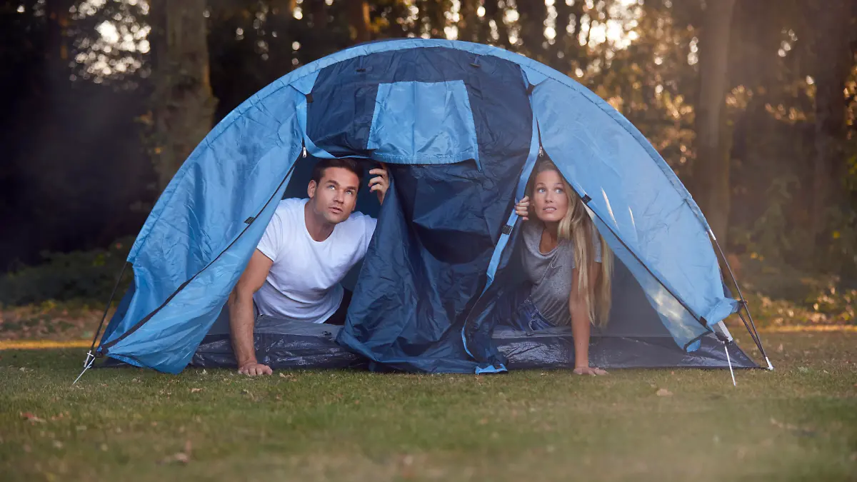 Couple Worried About Weather Looking Out Of Tent On Camping Trip In Countryside Together
