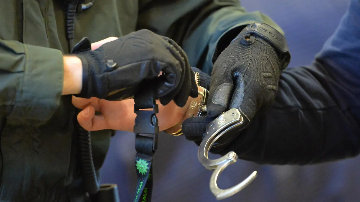 Ein Polizeibeamter nimmt beim Prozessbeginn gegen eine Thüringer Straßengang am 10.10.2013 in Erfurt (Thüringen) im Schwurgerichtssaal des Landgerichtes einem Angeklagten die Handschellen ab. Die insgesamt zehn Mitglieder der Gang im Alter von 22 bis 37 Jahren nannten sich selbst «Saat des Bösen» und sollen zahlreiche Straftaten begangenen haben. Die Bande soll in Suhl, Nordhausen, Weimar, Apolda und Gera aktiv gewesen sein. Bis Ende des Jahres sind 15 Verhandlungstermine angesetzt. Foto: Marc Tirl/dpa | Verwendung weltweit