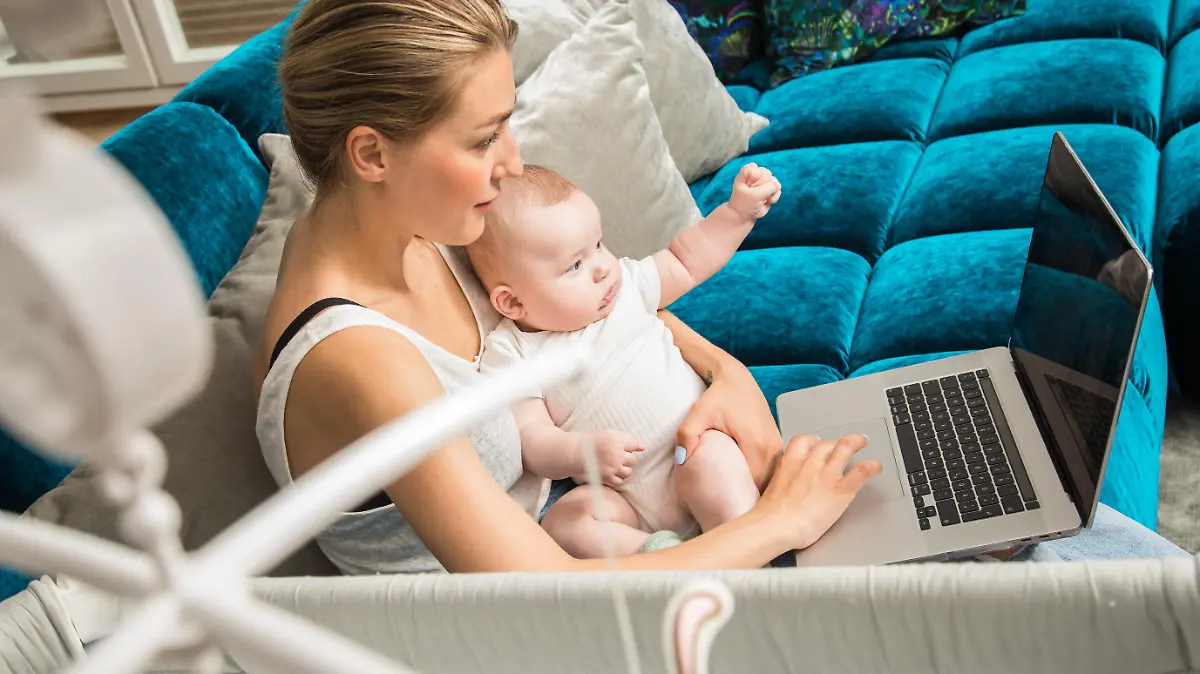 ILLUSTRATION - Eine Frau haelt am 24.06.2021 in Berlin ihr Baby auf dem Schoss, waehrend sie an einem Laptop arbeitet (gestellte Szene). Foto: Christin Klose