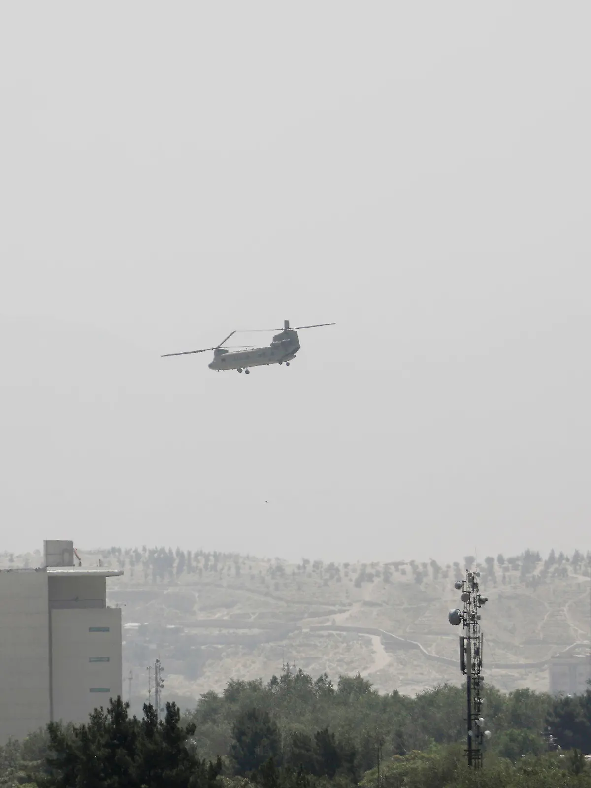 A U.S. Chinook helicopter flies over the U.S. Embassy, left, in Kabul, Afghanistan, Sunday, Aug. 15, 2021. Helicopters are landing at the U.S. Embassy in Kabul as diplomatic vehicles leave the compound amid the Taliban advanced on the Afghan capital. (AP Photo/Rahmat Gul)